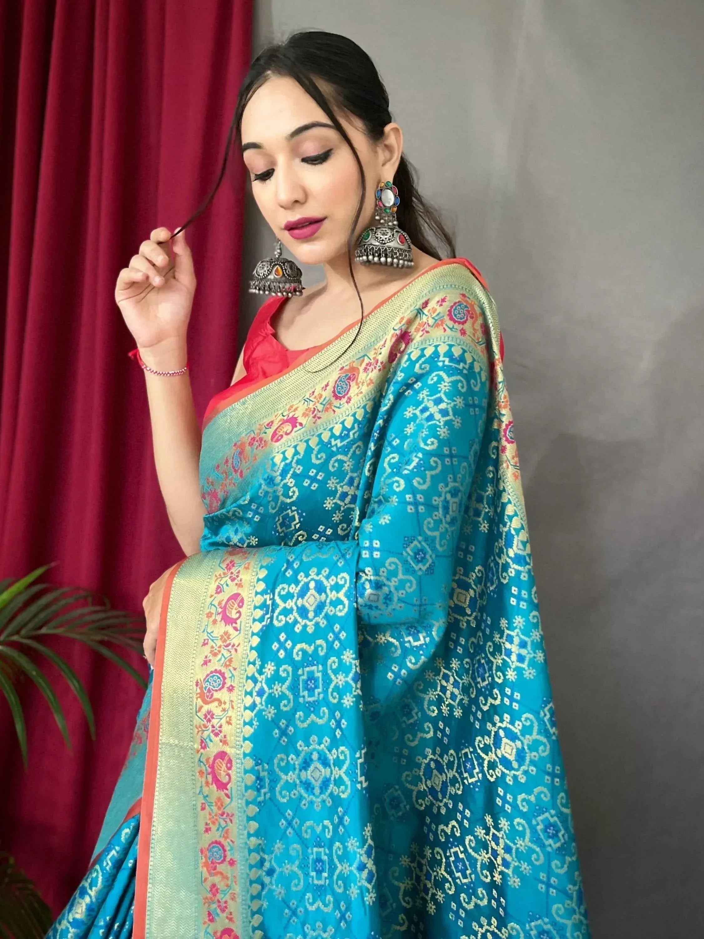Woman in vibrant blue Indian saree with gold patterns, red blouse, and jhumka earrings, styled for ethnic occasions.