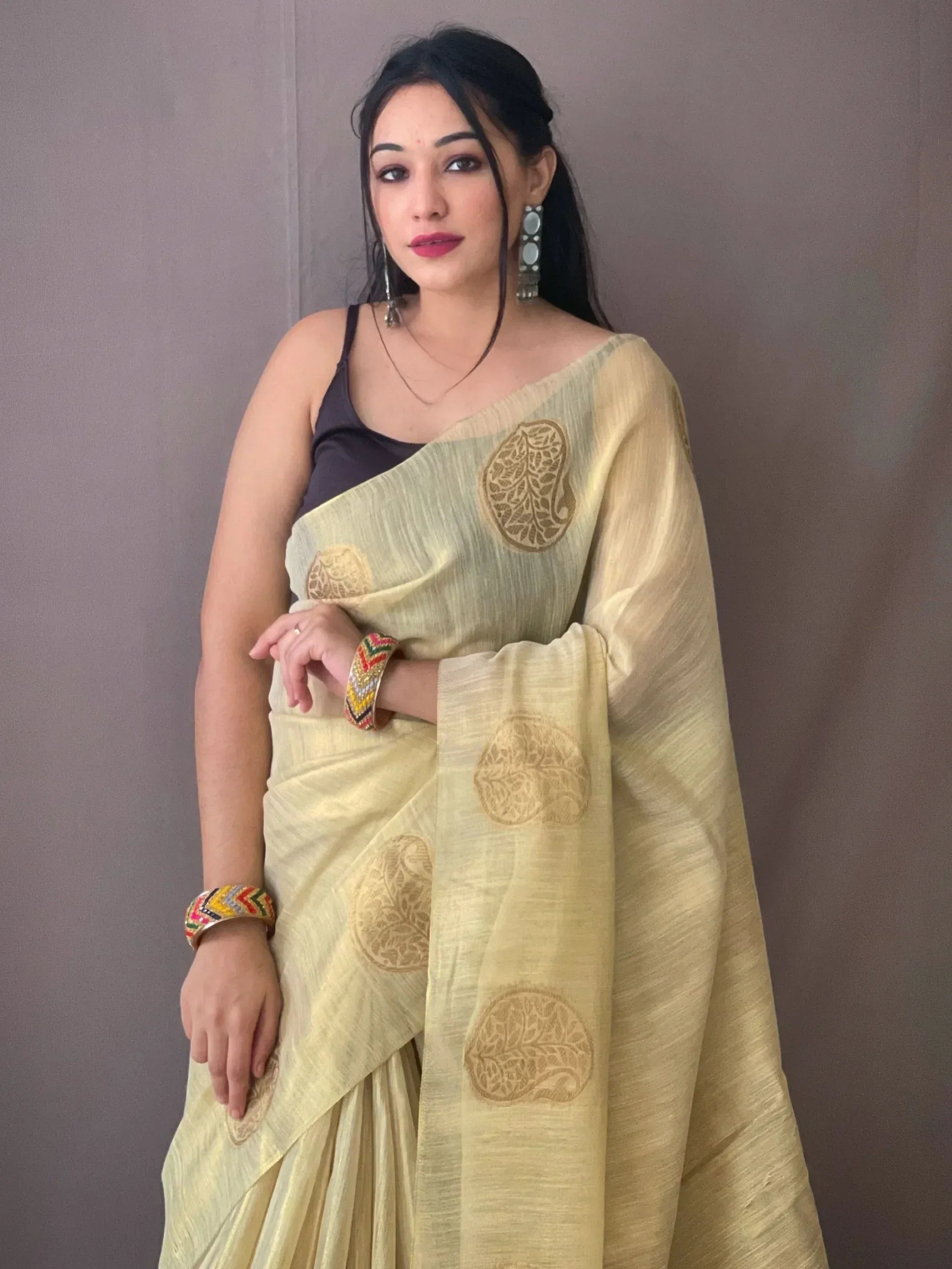 Woman in light yellow saree with gold leaf motifs, ethnic Indian wear, paired with colorful bangles and statement earrings