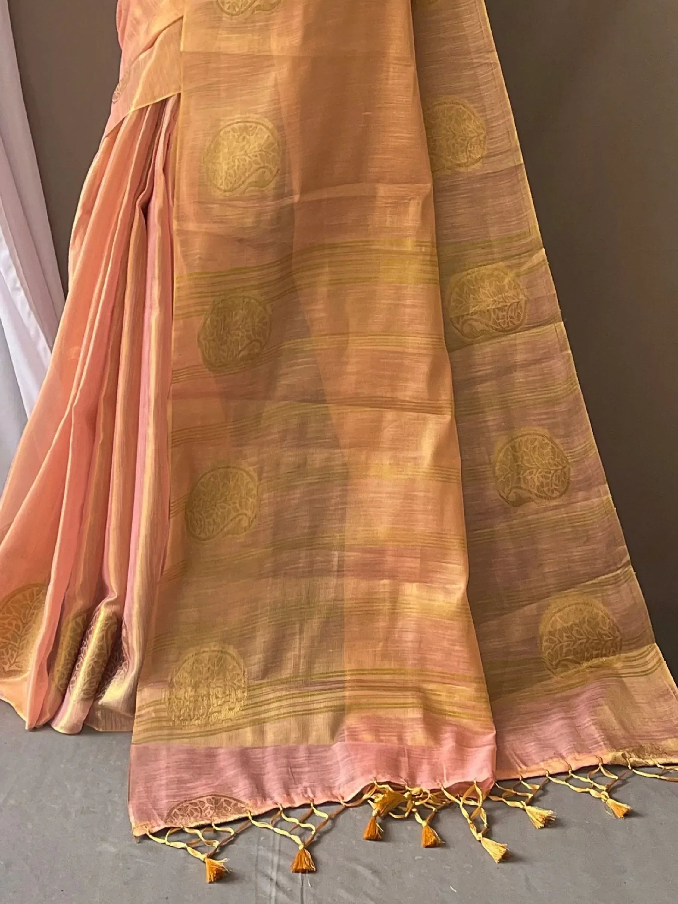 Peach and gold designer saree with floral motifs and tassels, ideal for ethnic wear occasions