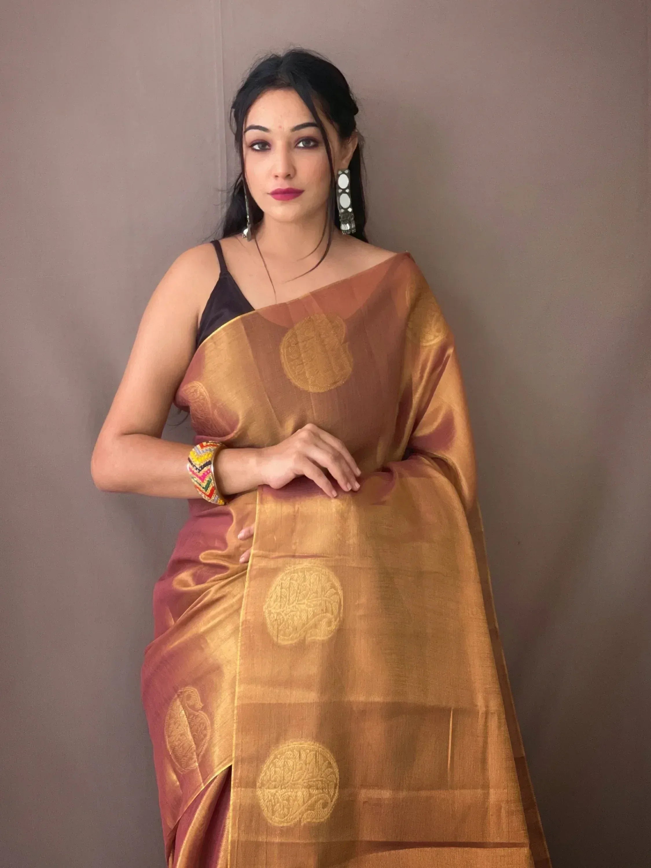 Woman wearing elegant golden-brown ethnic saree with circular motifs, styled with black blouse and statement earrings