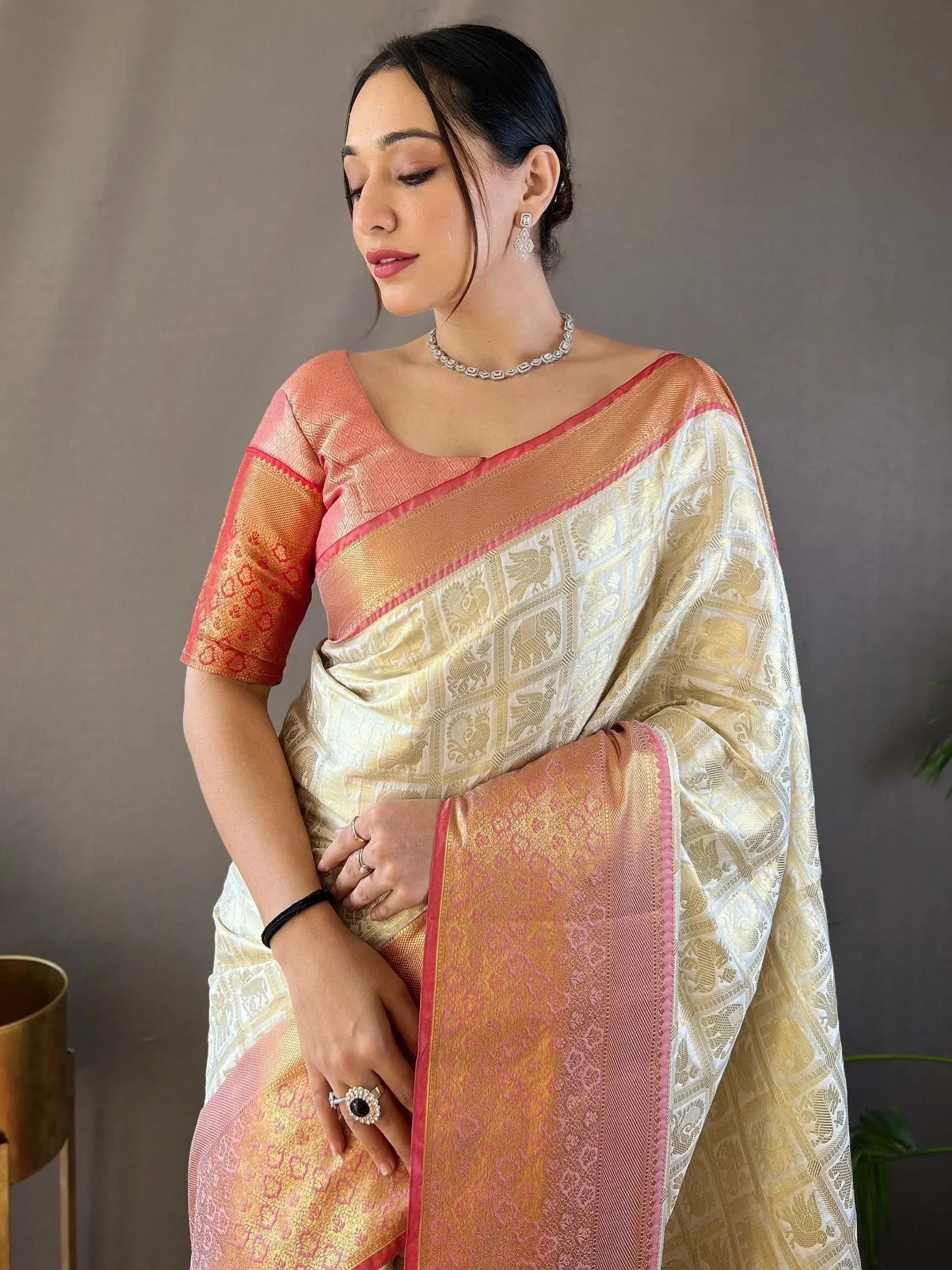Elegant cream and peach Banarasi saree with gold elephant motifs and pink border, paired with matching blouse.
