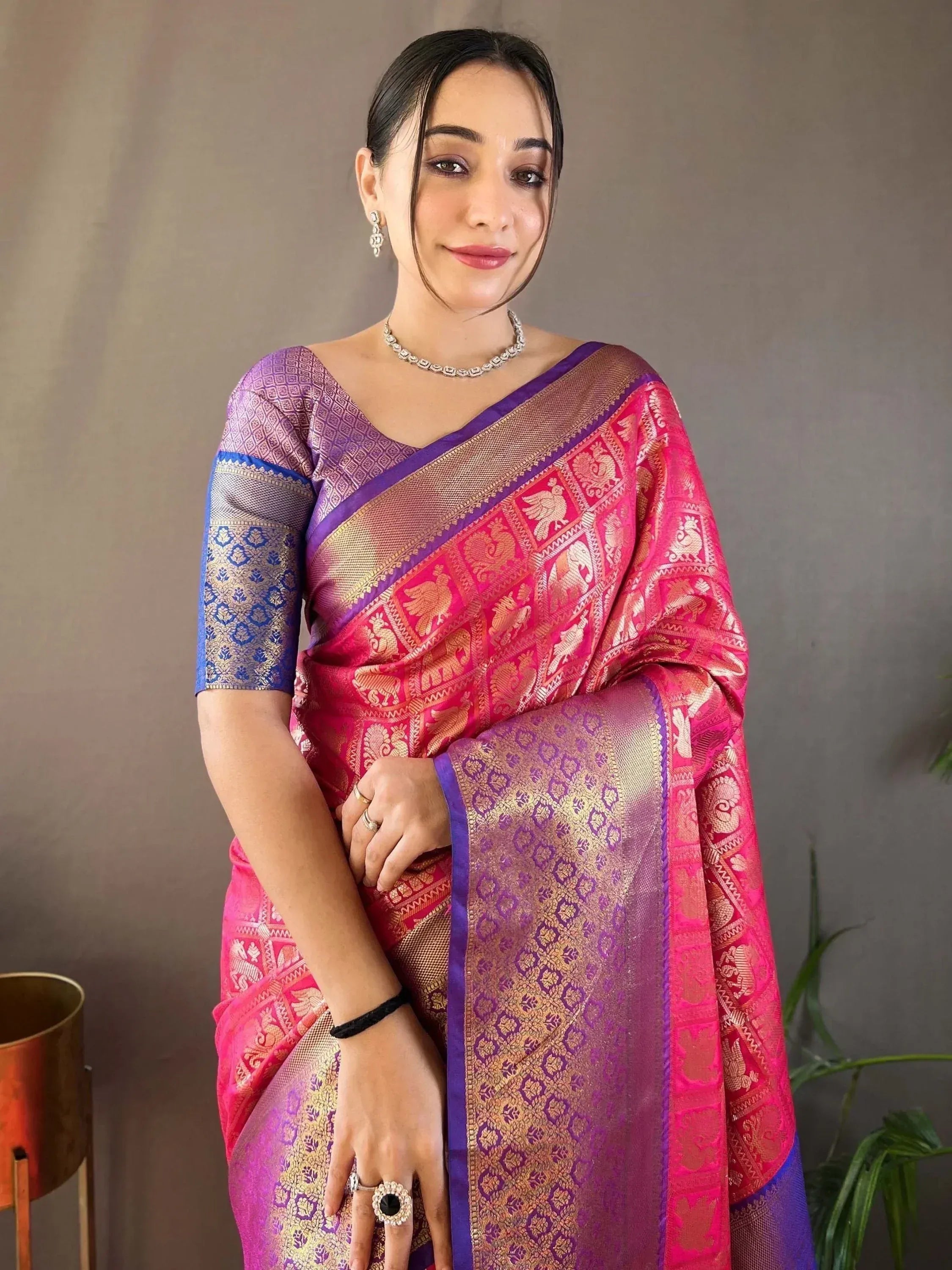 Woman in vibrant pink and purple designer saree with gold zari work, perfect for Indian ethnic occasions.