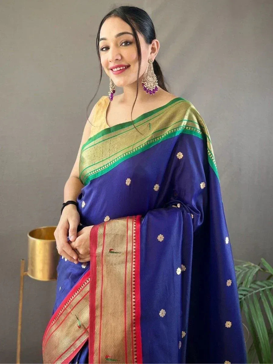 Woman in royal blue saree with gold and green border, floral motifs, and traditional earrings