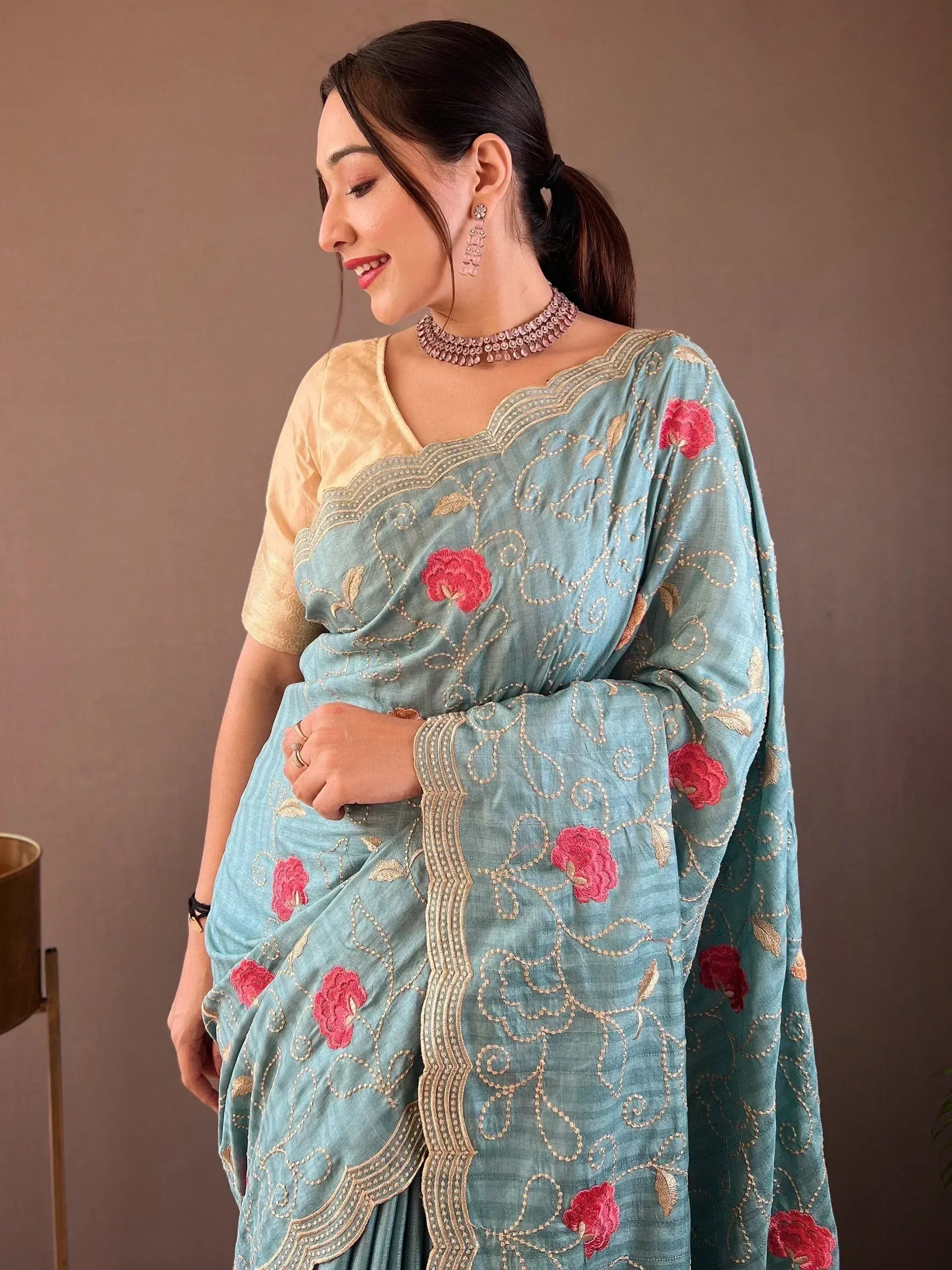 Woman in blue embroidered saree with pink floral design, gold blouse, and ethnic jewelry