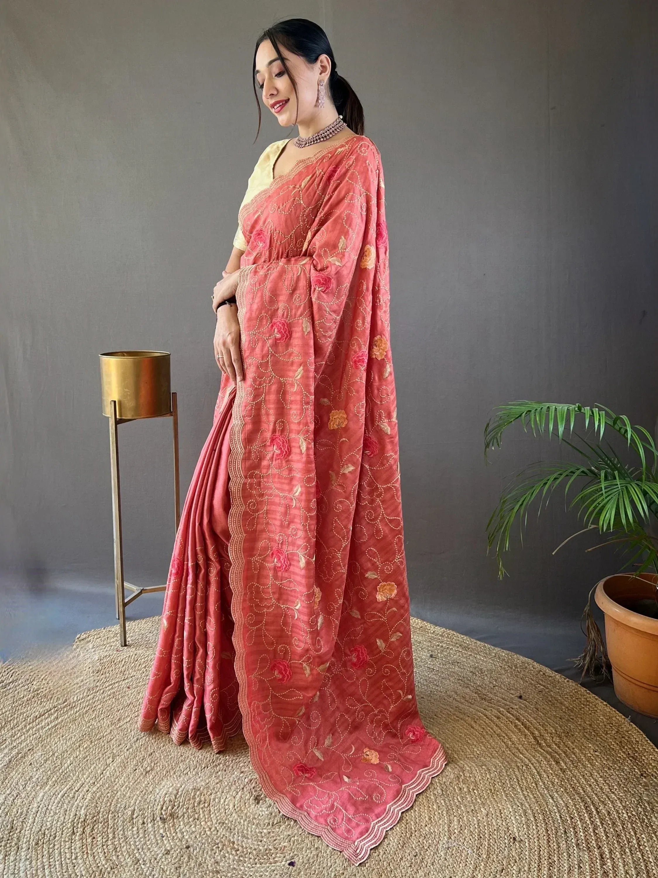 Woman in coral pink embroidered saree with floral motifs, paired with yellow blouse, ideal for ethnic occasions
