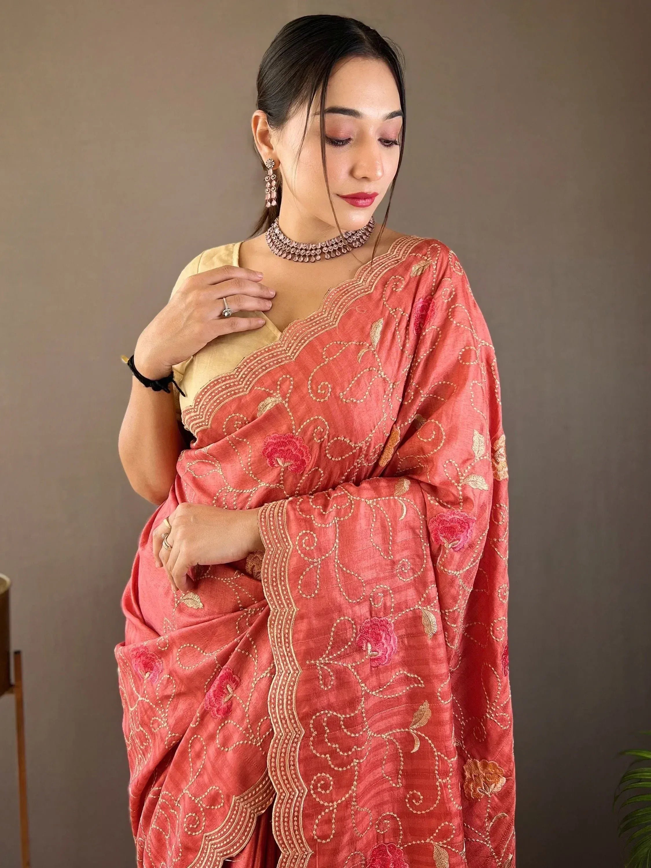 Woman in coral embroidered saree with gold floral motifs and matching blouse, styled with choker and earrings