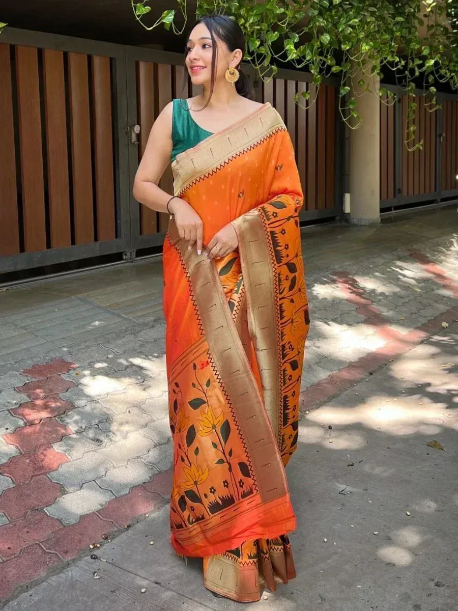 Woman in orange floral print saree with gold border, paired with green blouse, outdoor setting
