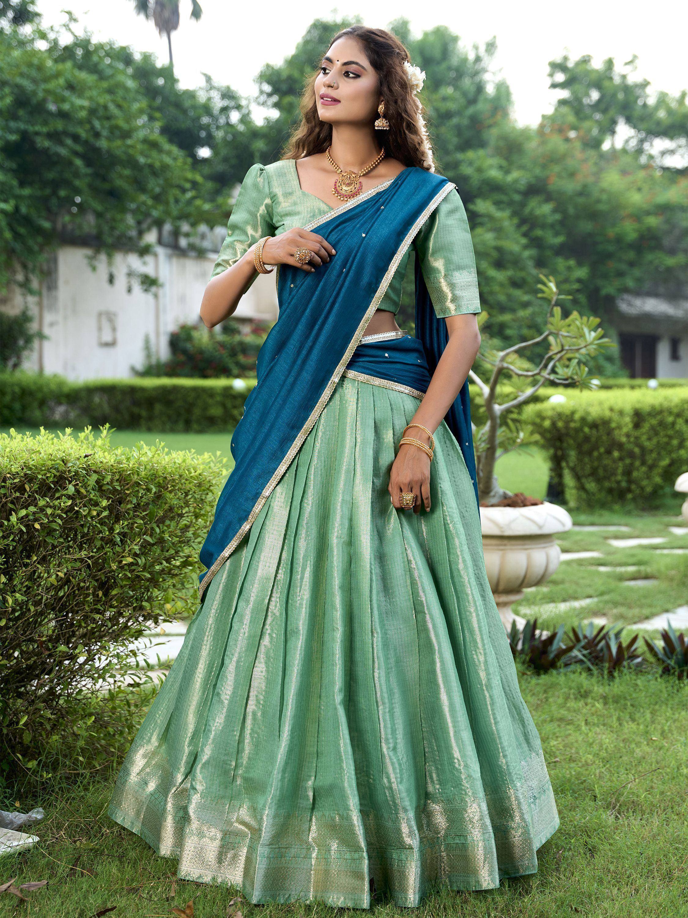 Green and teal lehenga choli with gold trim, styled with traditional jewelry in a garden setting
