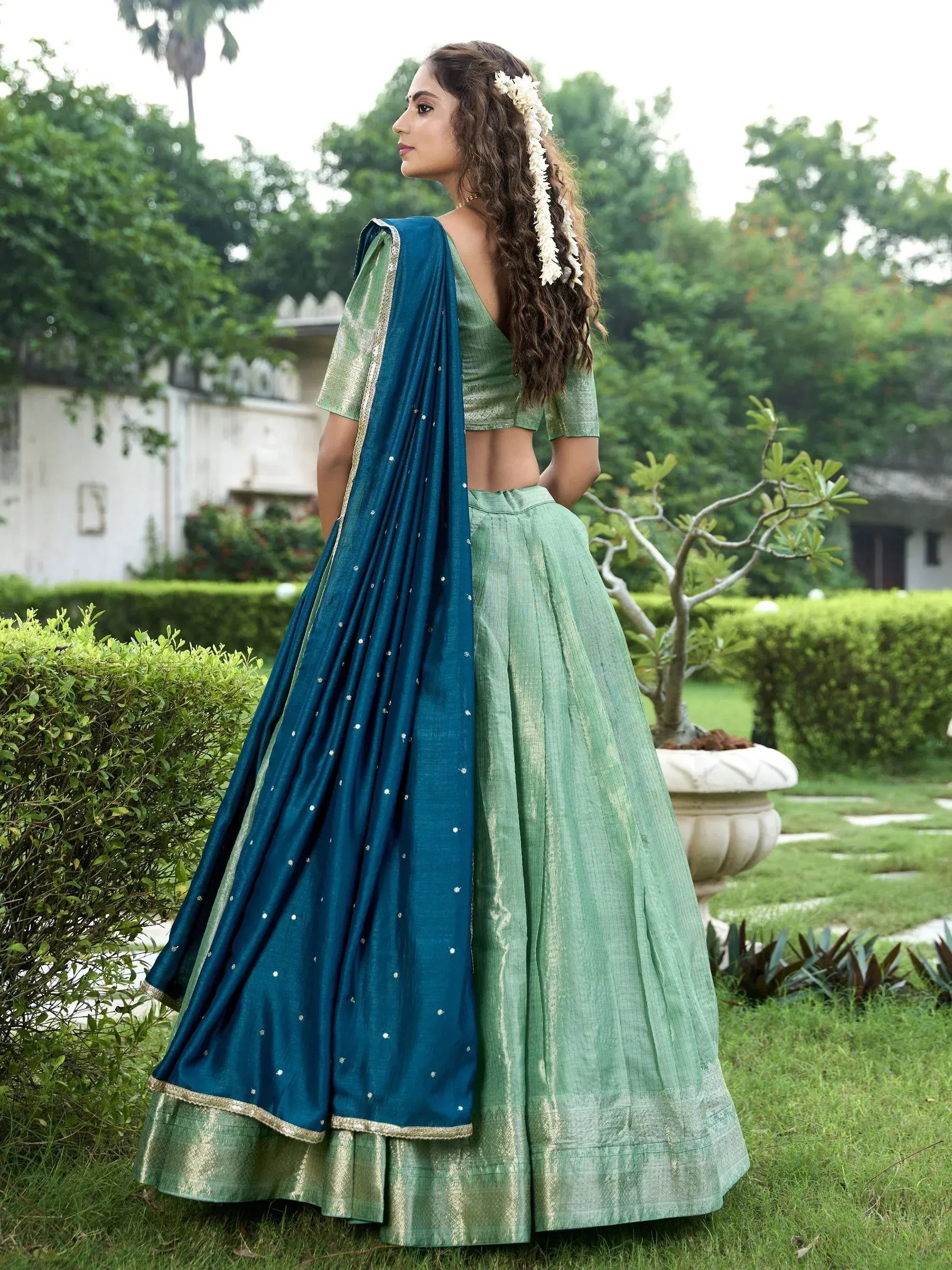 Green lehenga choli with blue dupatta, ethnic Indian wear for women, floral hair accessory, garden setting
