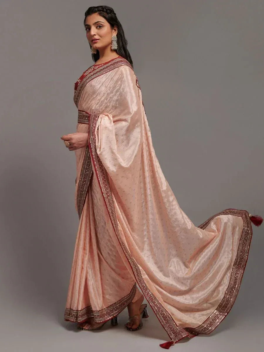 Elegant peach saree with red border and gold embroidery, styled with statement earrings for festive occasions
