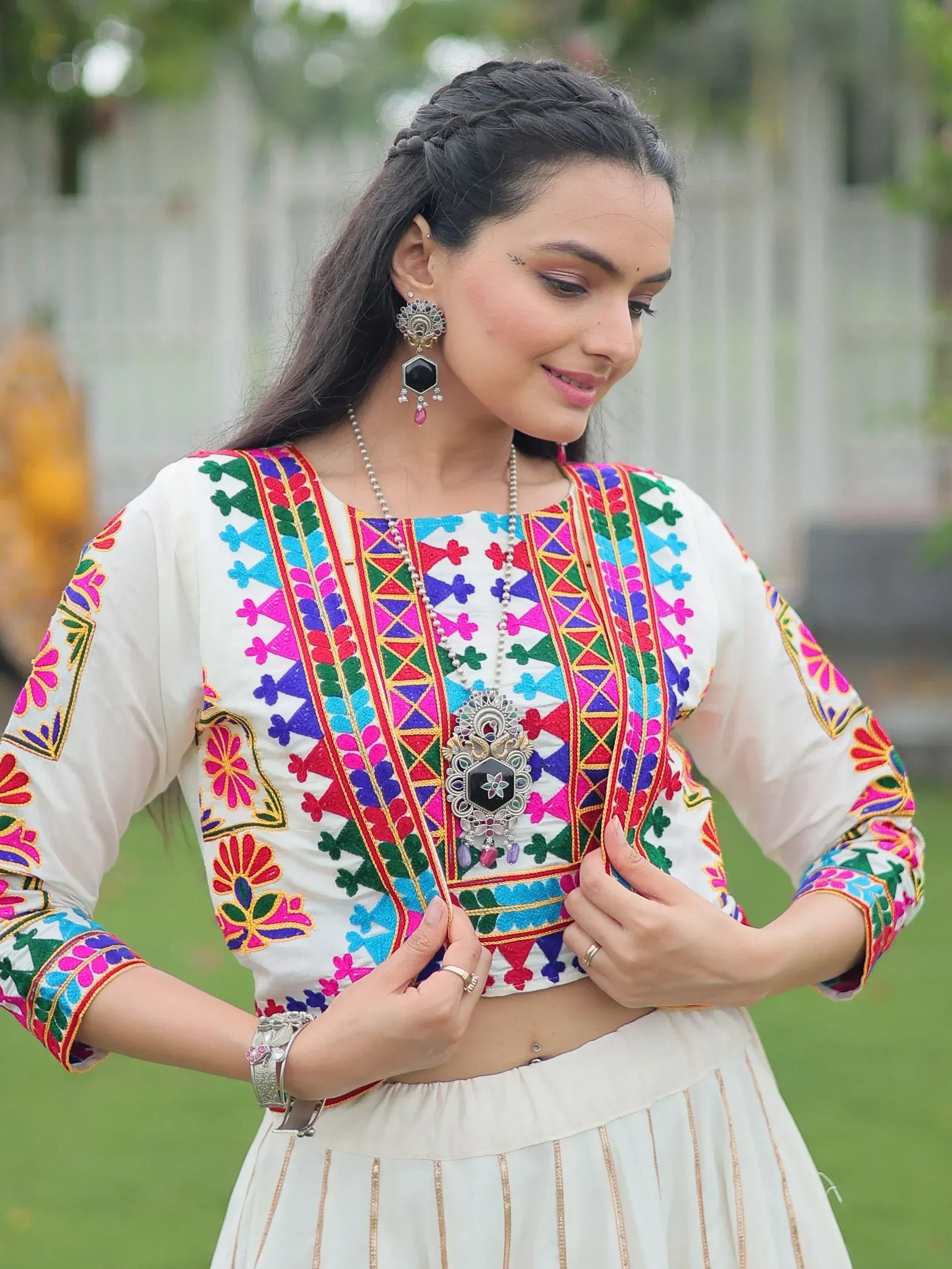 Woman in white ethnic crop top with colorful embroidery and matching skirt, styled with traditional jewelry
