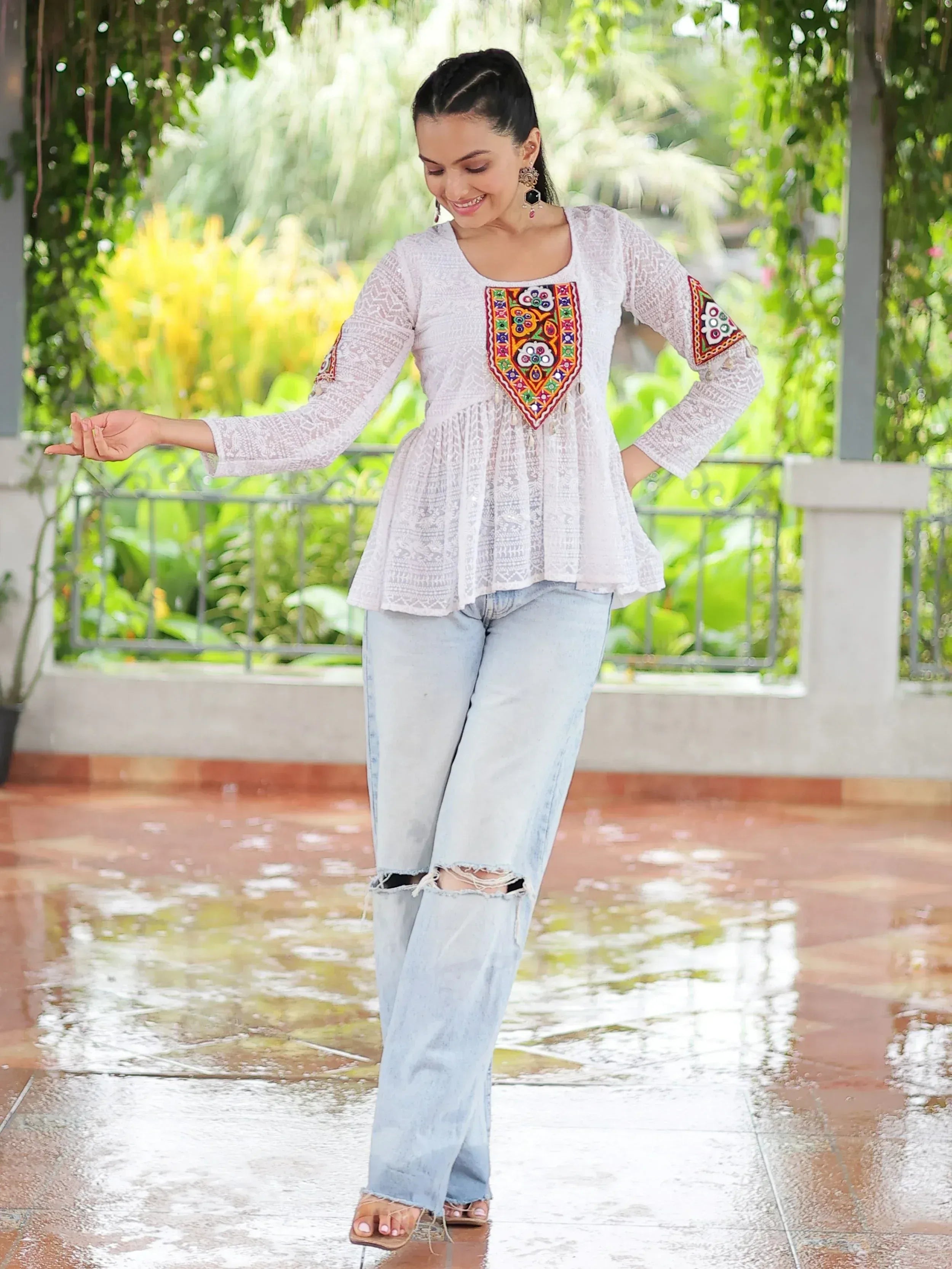 White embroidered ethnic top with colorful mirror work, paired with ripped jeans, perfect for casual Indian wear.