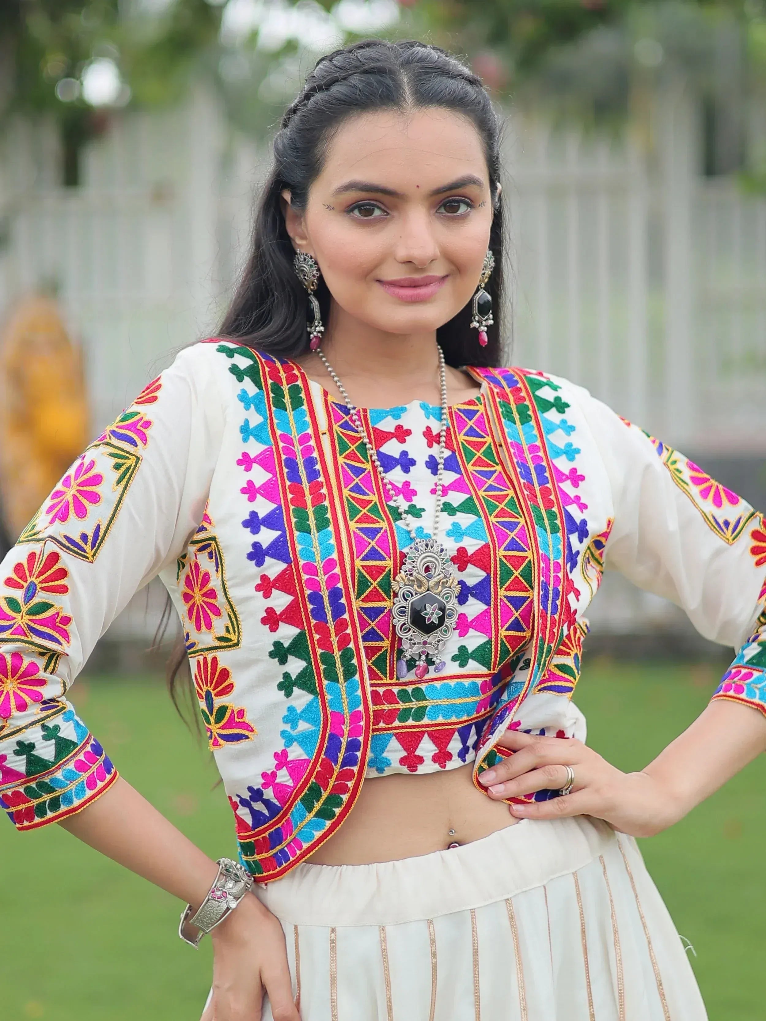 Woman in white embroidered ethnic crop top with colorful floral patterns and matching skirt, styled with traditional jewelry