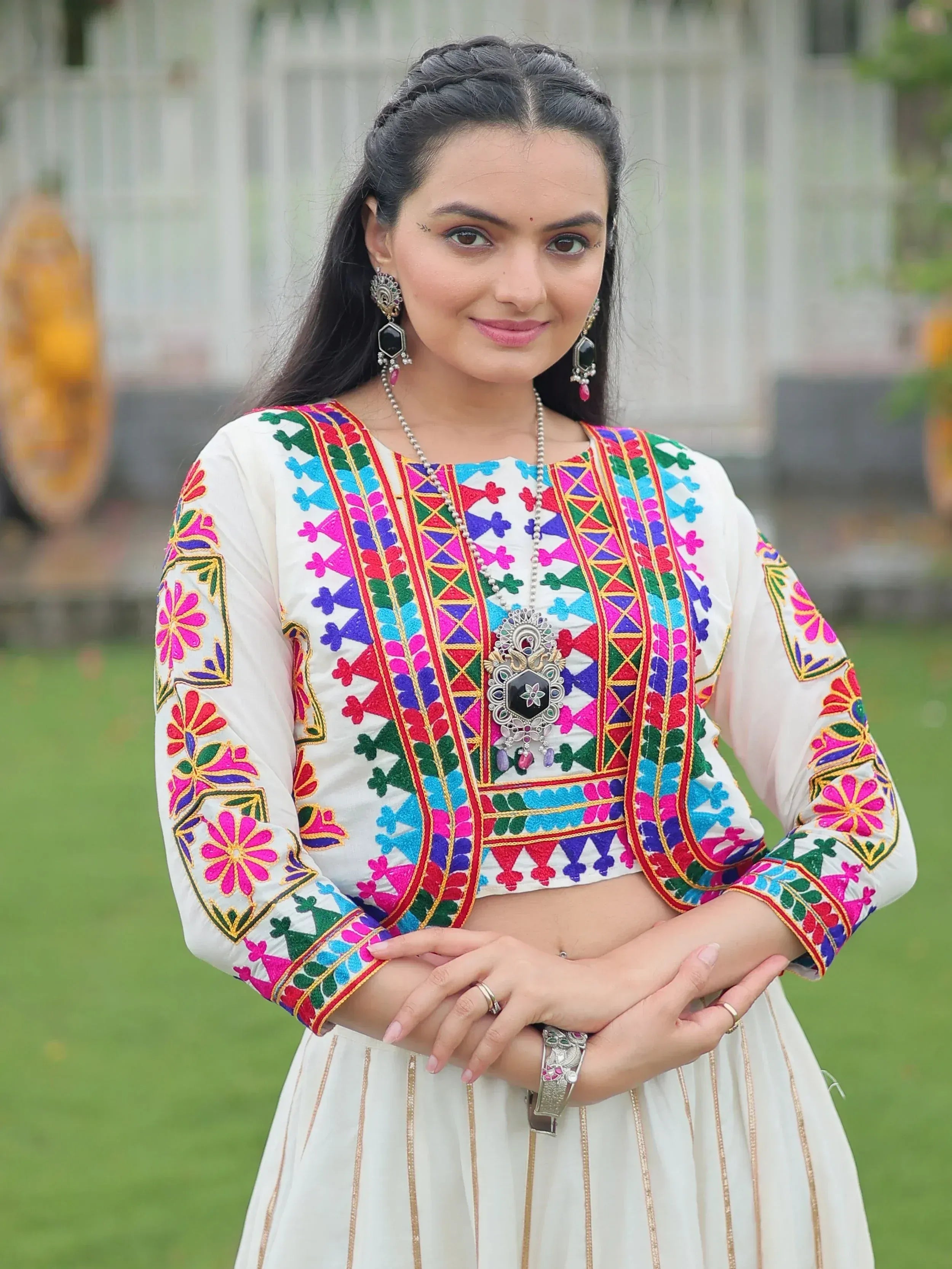 White embroidered ethnic crop top with colorful floral patterns, paired with matching skirt and traditional jewelry