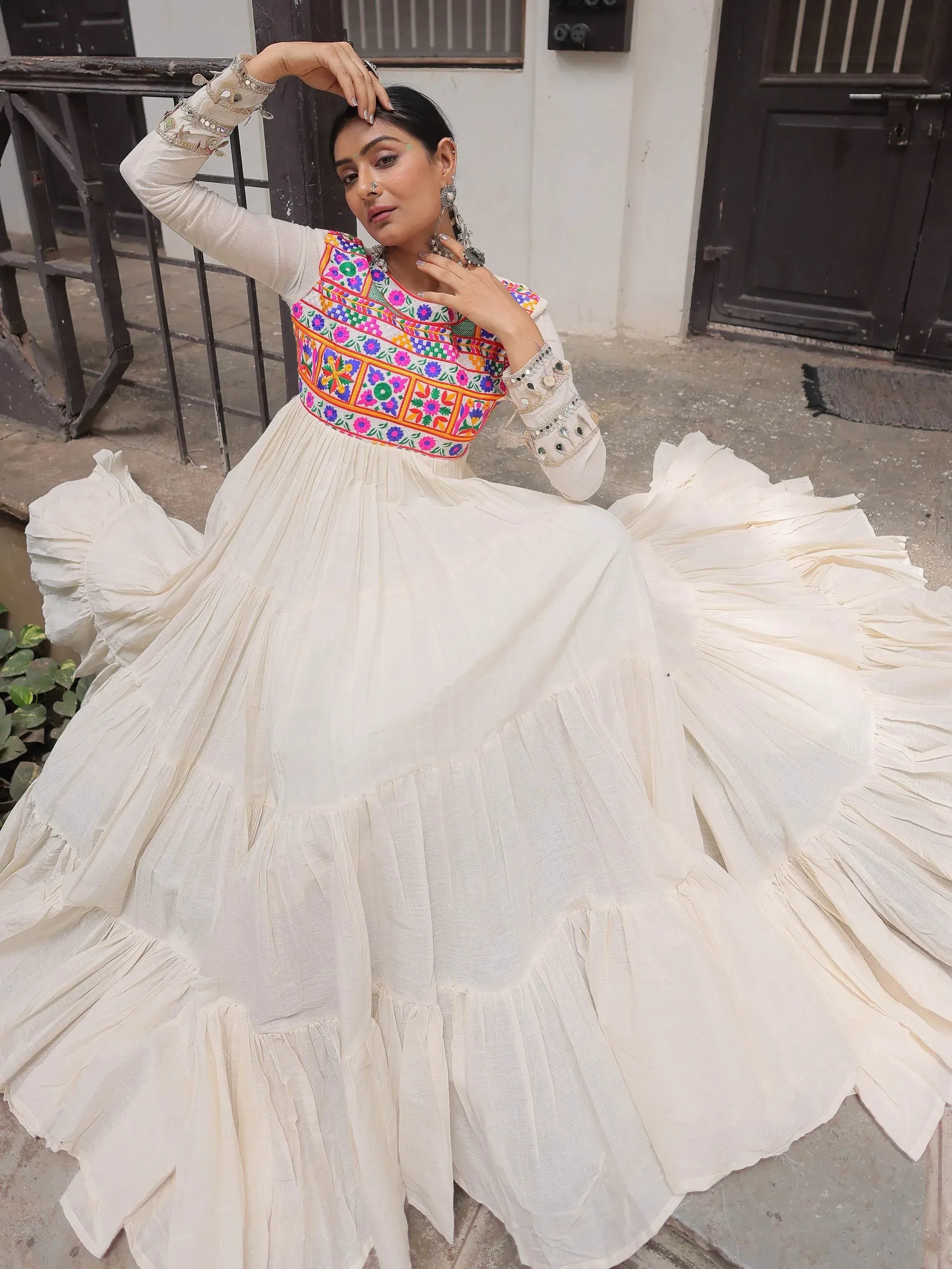 White ethnic gown with colorful floral embroidery and mirror work, perfect for Indian festive occasions.