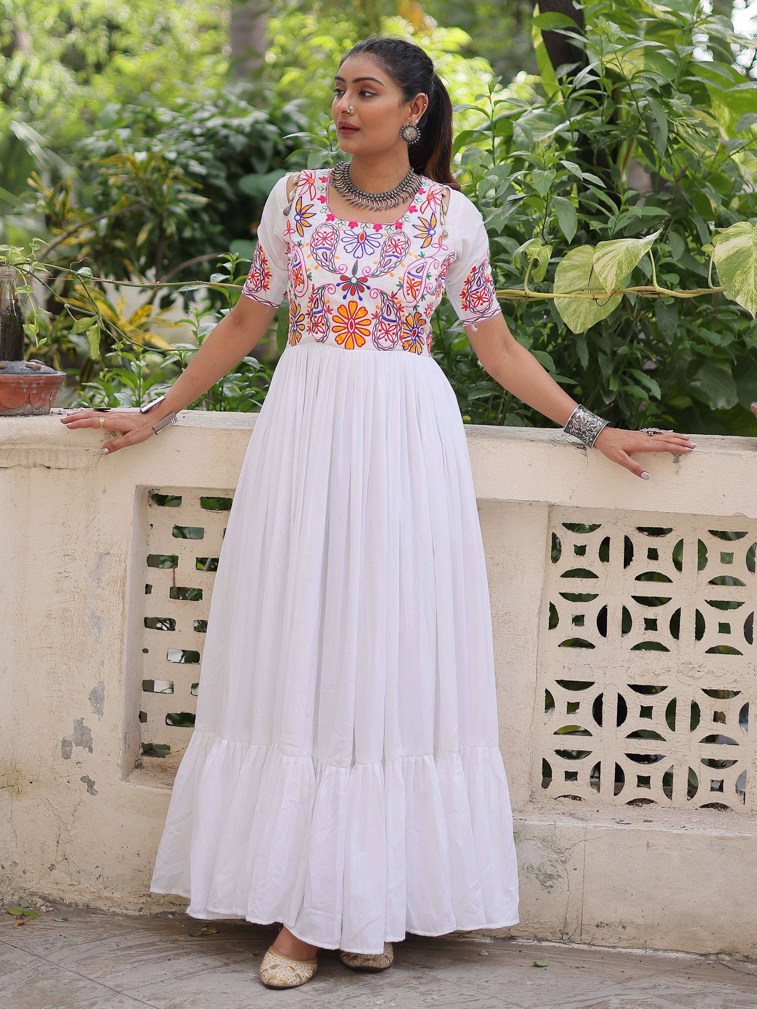 Woman in white embroidered ethnic gown with floral patterns, accessorized with traditional jewelry.