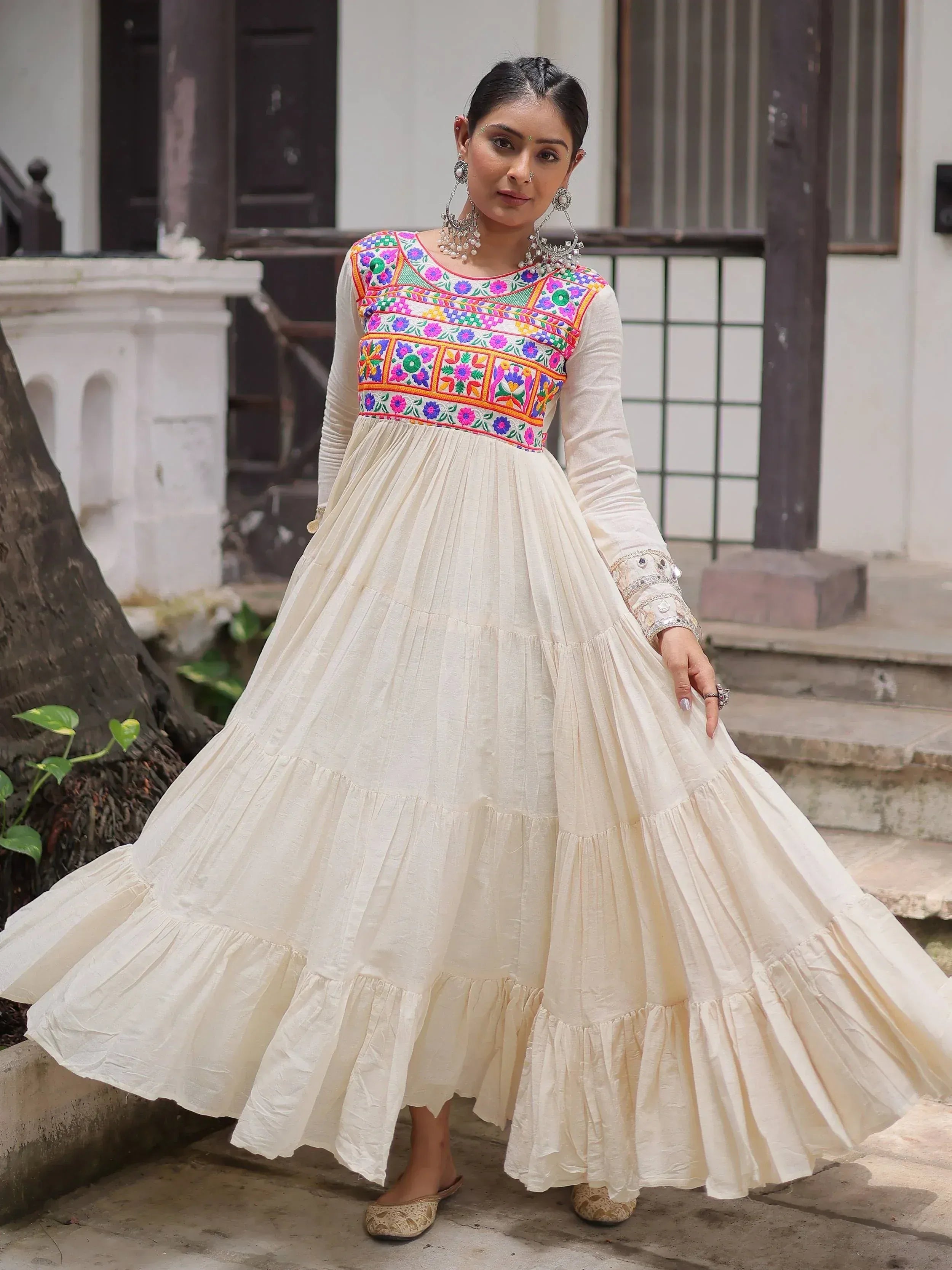 Cream ethnic gown with colorful floral embroidery, long sleeves, tiered skirt, perfect for Indian occasions