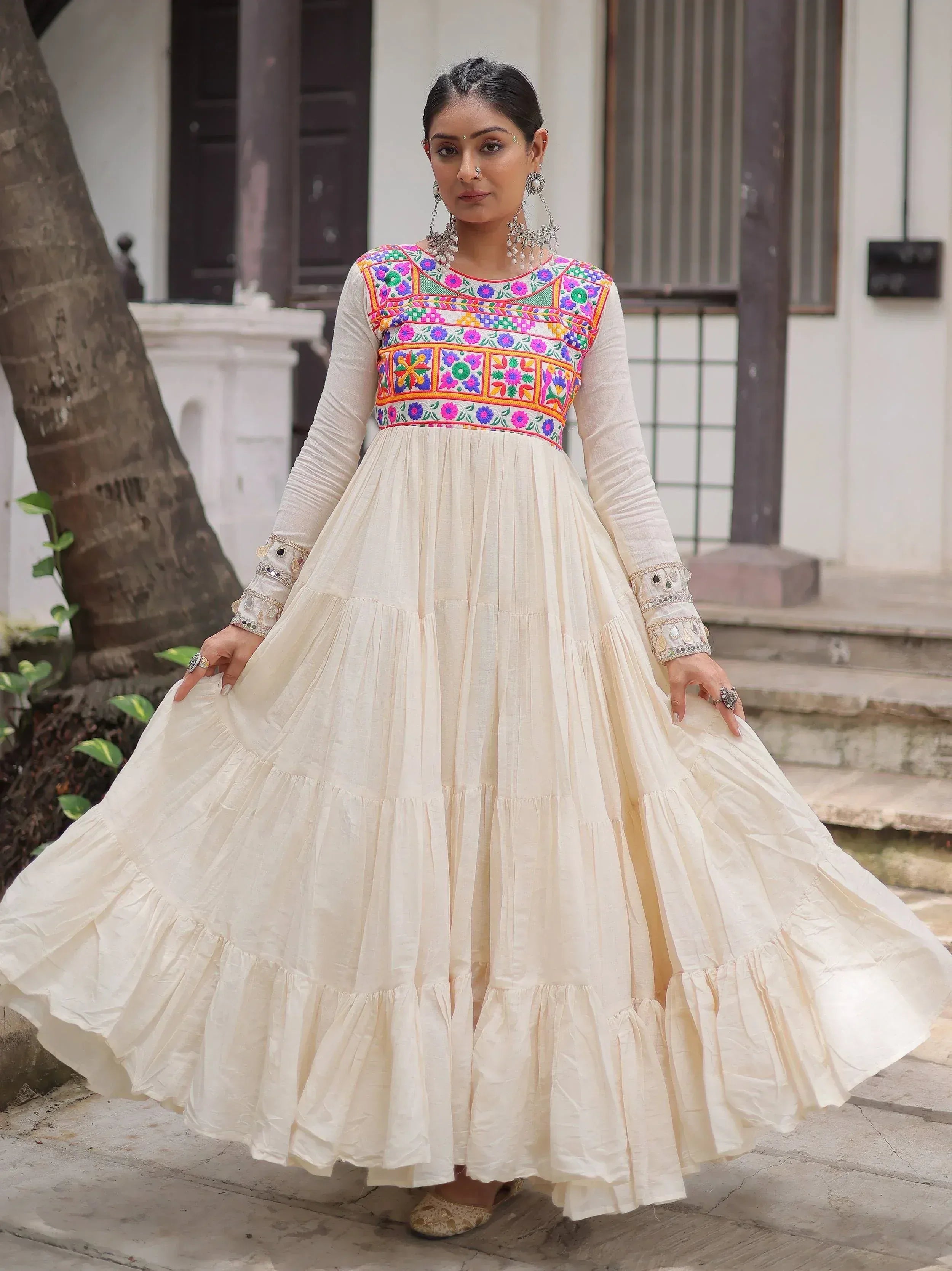 Cream ethnic gown with colorful floral embroidery, long sleeves, and tiered skirt for Indian occasions
