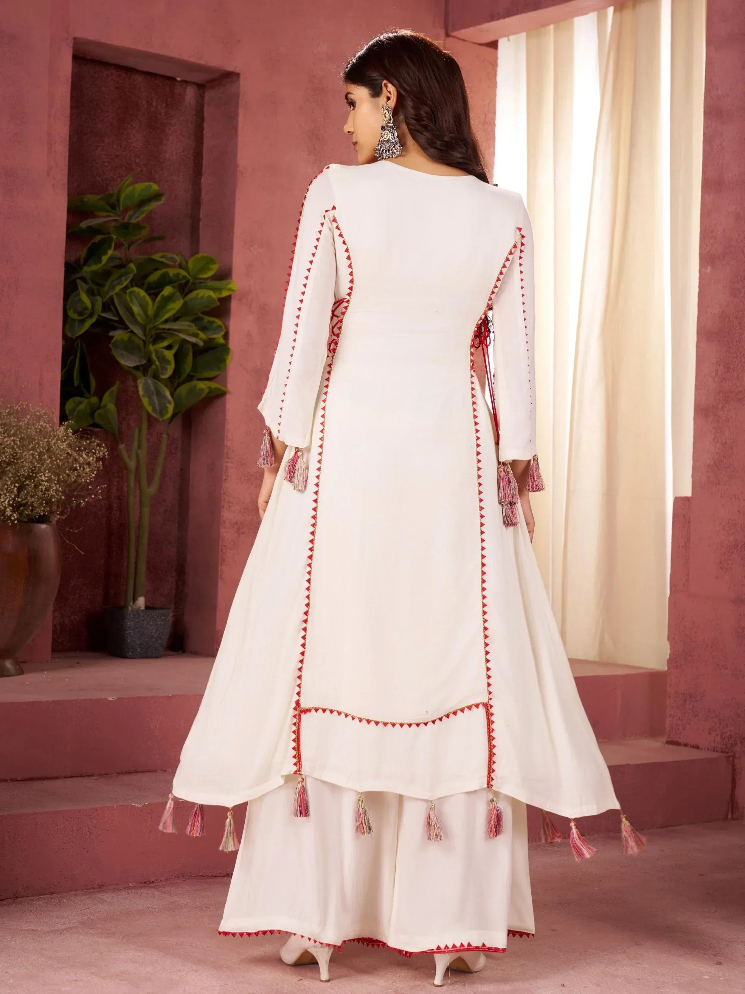 White ethnic anarkali with red embroidery and tassels, paired with palazzo pants, ideal for Indian festive occasions.