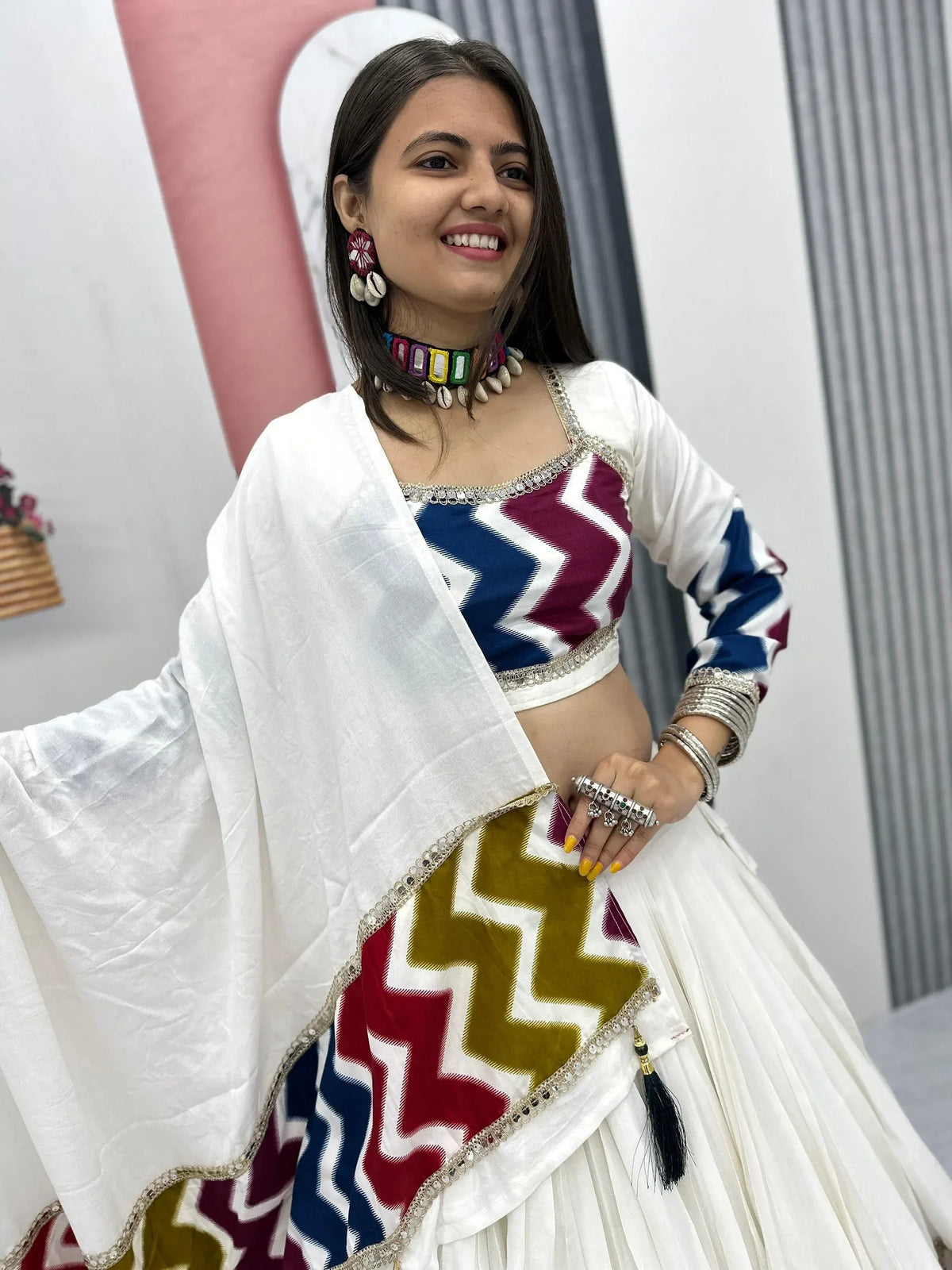 Woman in white lehenga choli with colorful zigzag print, ethnic jewelry, and dupatta for Indian festive wear