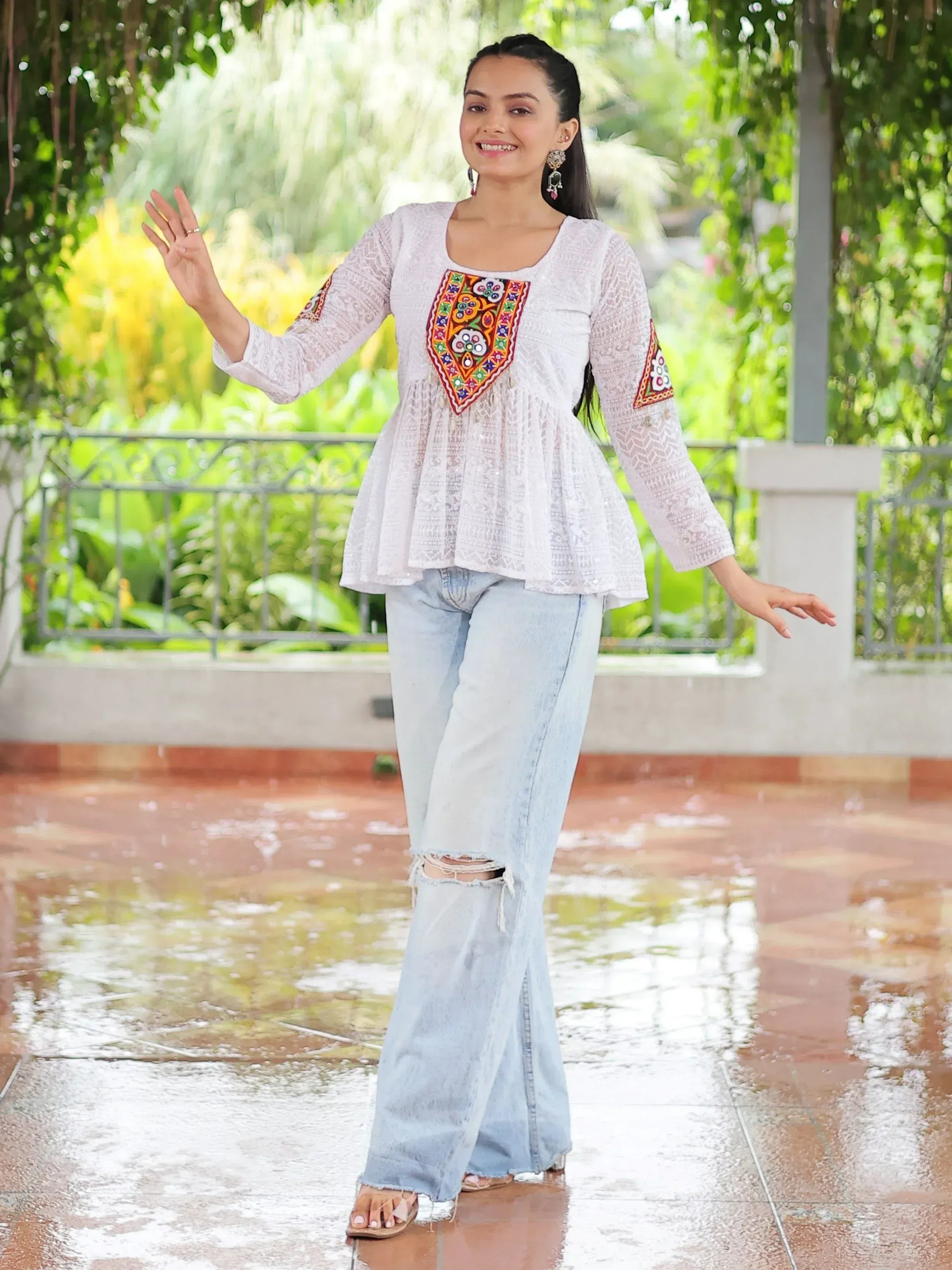 White embroidered ethnic top with colorful mirror work, paired with ripped denim jeans, perfect for casual Indian wear.