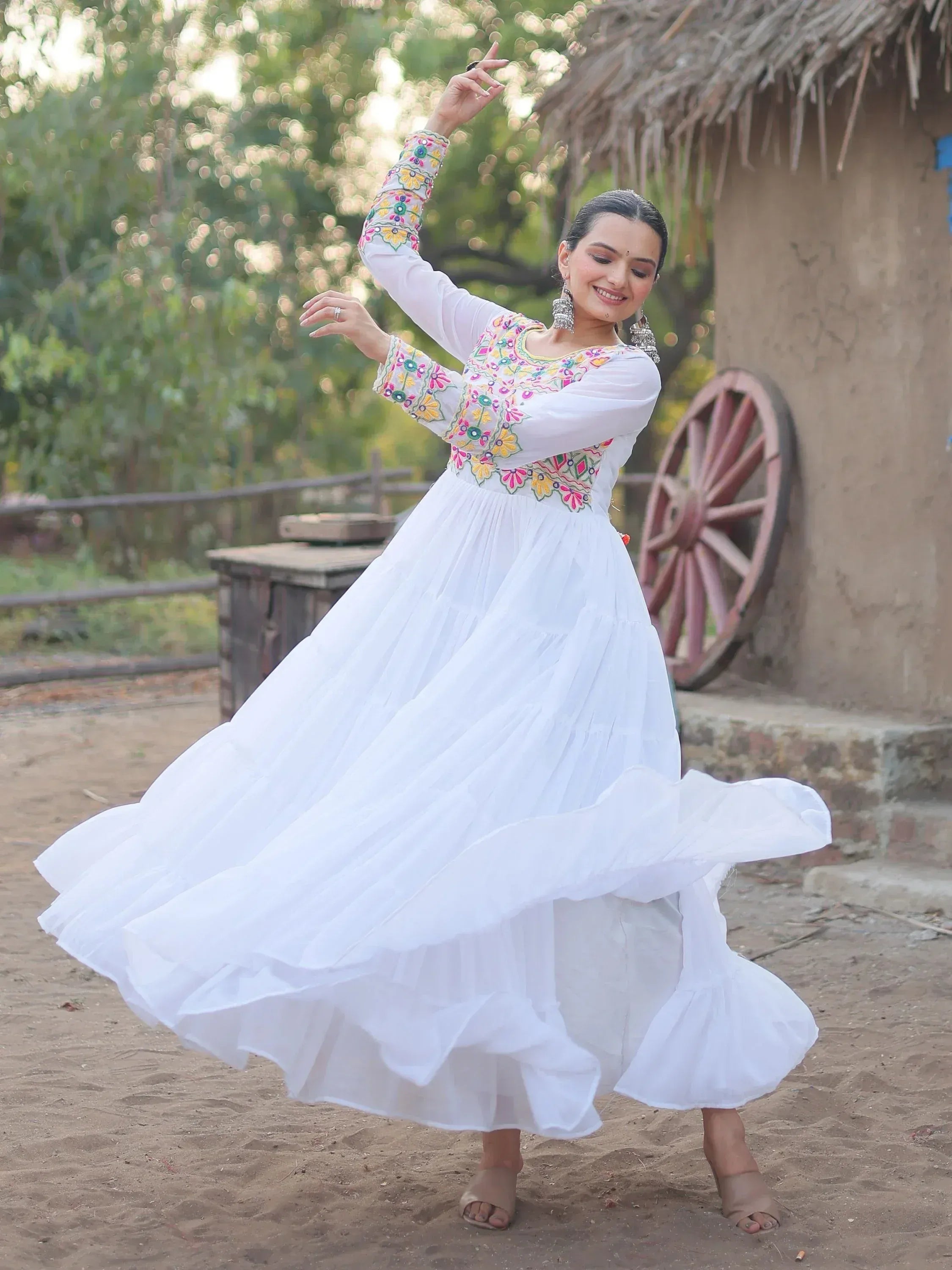 Woman in white embroidered ethnic gown dancing outdoors near rustic hut