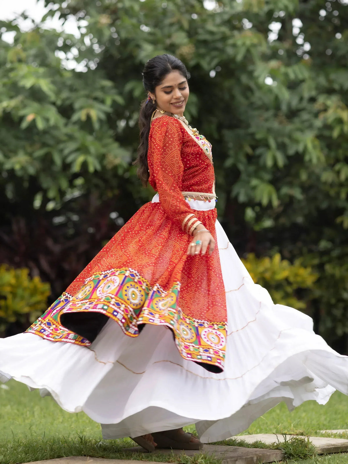 Woman in red and white ethnic Indian dress with mirror work, twirling outdoors