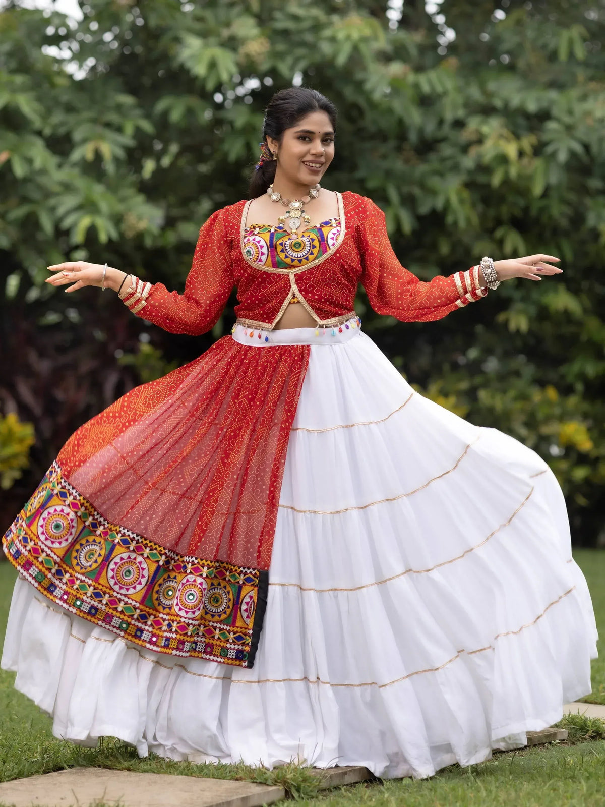 Woman in vibrant red and white ethnic lehenga choli with mirror work, dancing outdoors