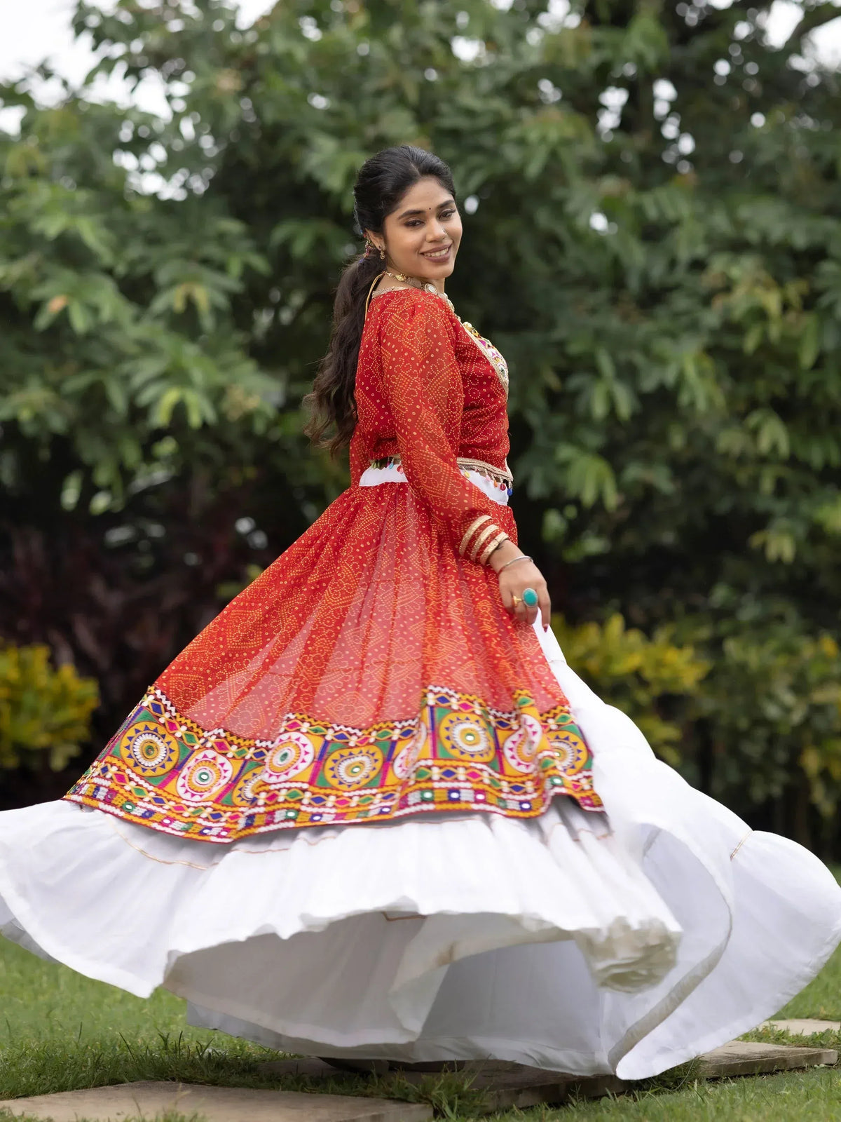 Woman in vibrant red and white ethnic Anarkali with colorful embroidery, twirling outdoors