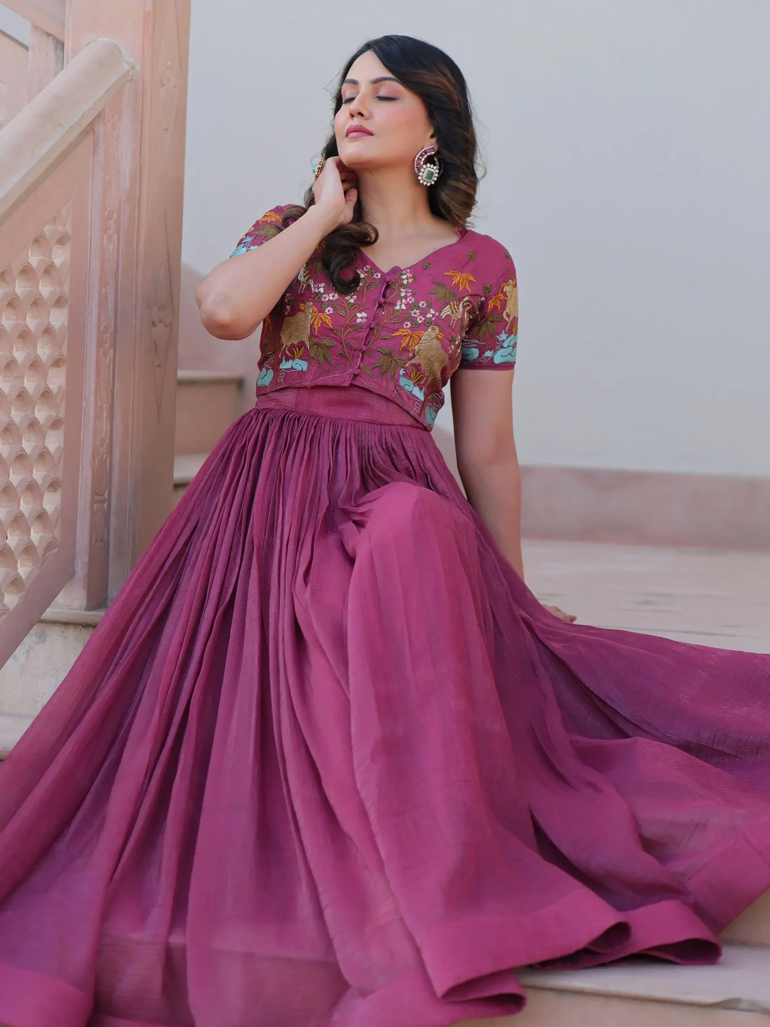 Woman in maroon embroidered ethnic gown with floral and animal motifs, styled with statement earrings