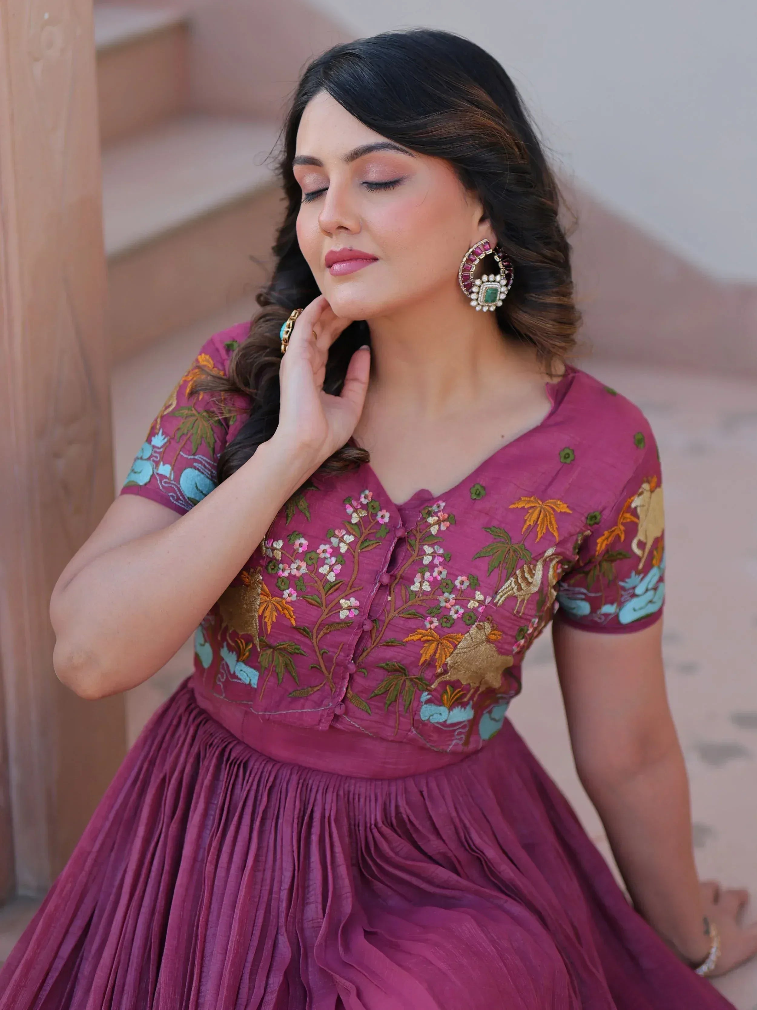 Woman in maroon embroidered ethnic gown with floral and animal motifs, styled with statement earrings