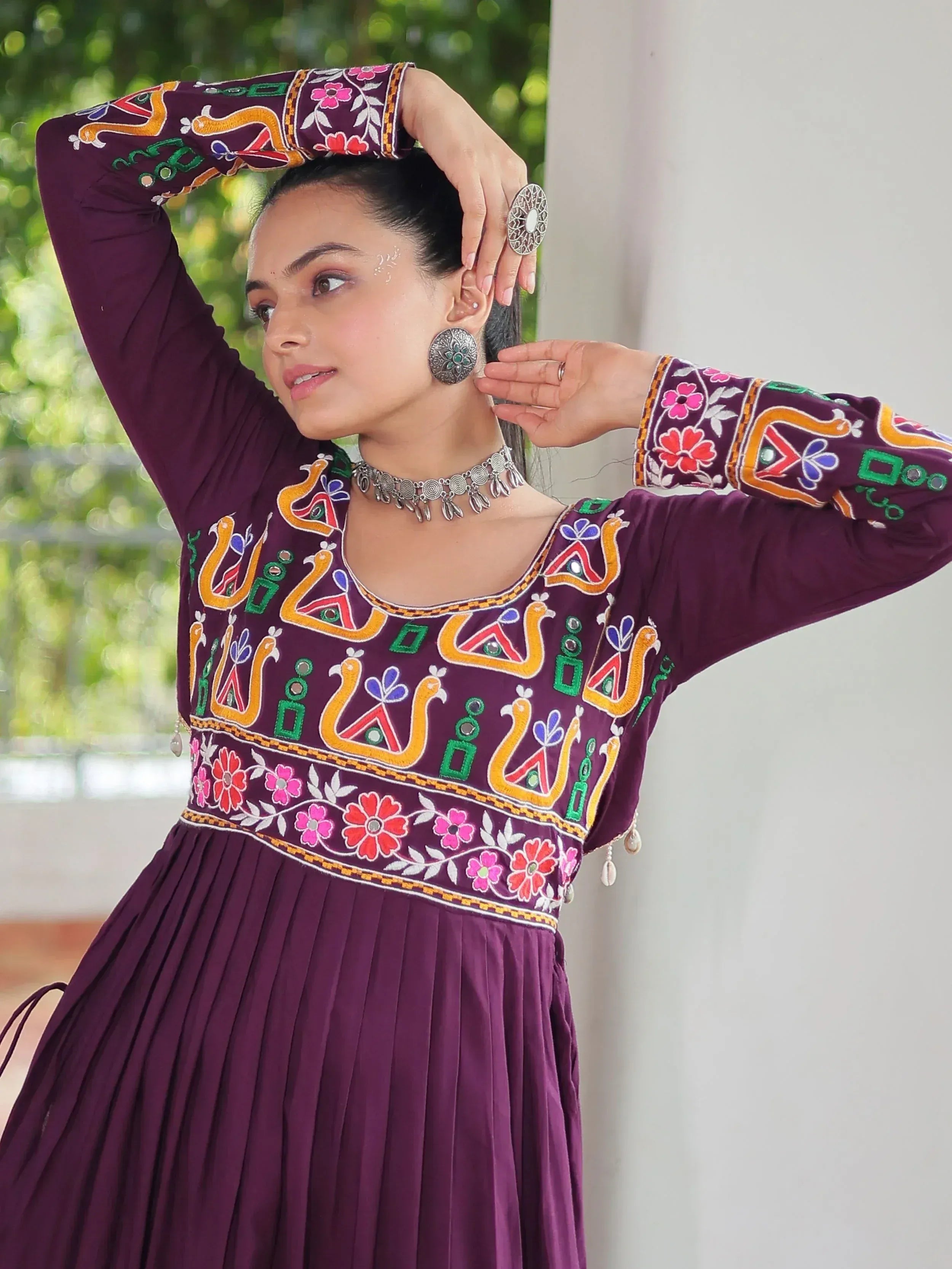Woman in purple embroidered ethnic gown with floral and peacock motifs, silver jewelry, outdoor setting