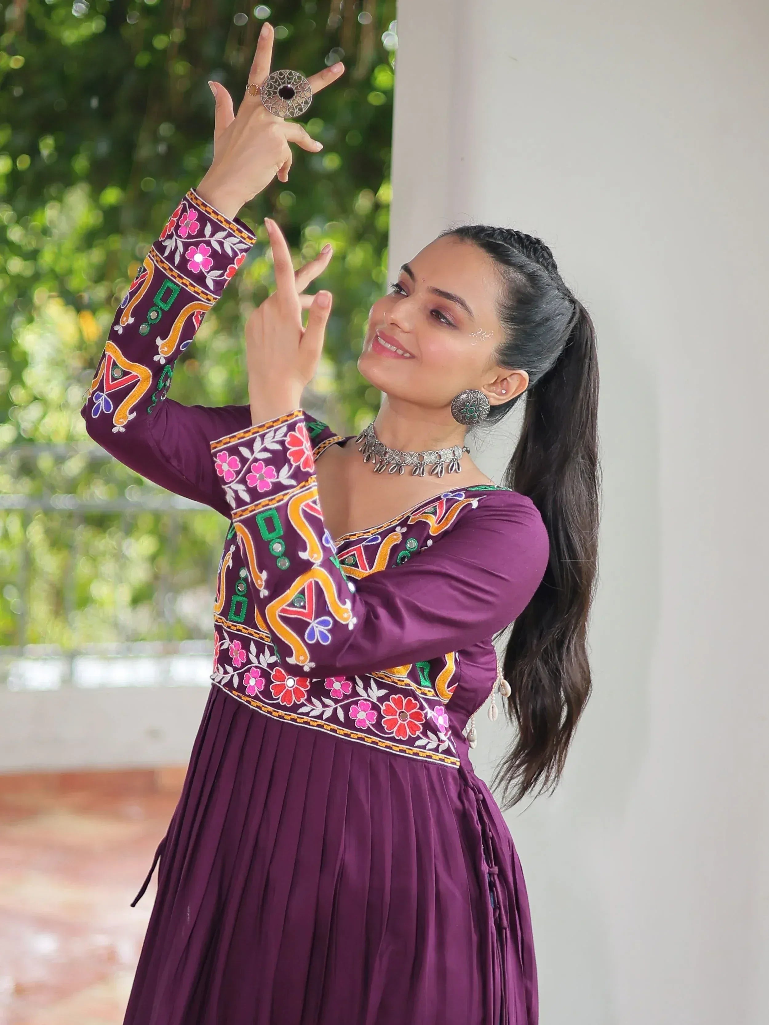 Woman in purple embroidered ethnic gown with floral patterns, posing outdoors