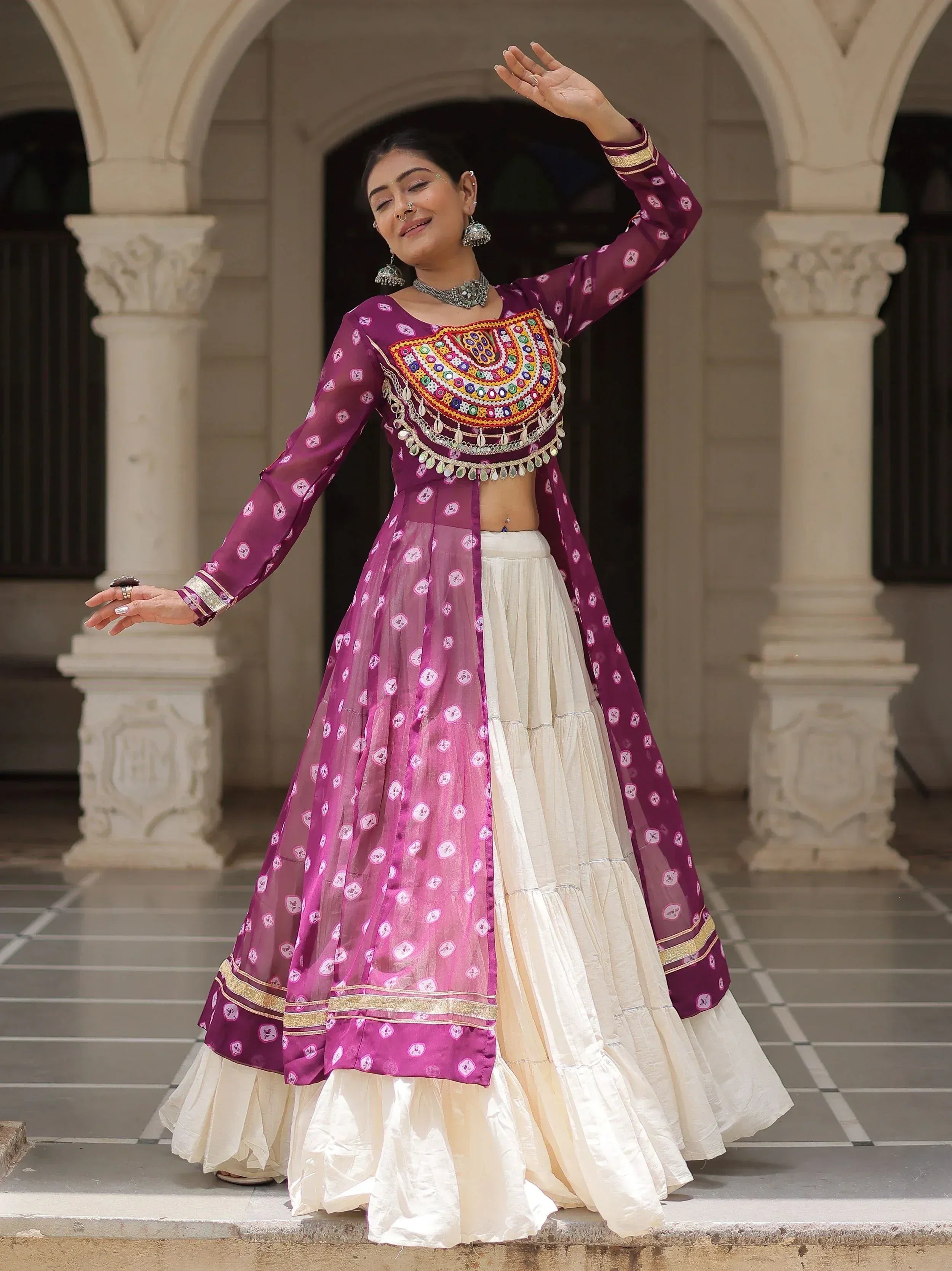 Woman in purple and cream ethnic lehenga choli with mirror work, dancing under arched courtyard