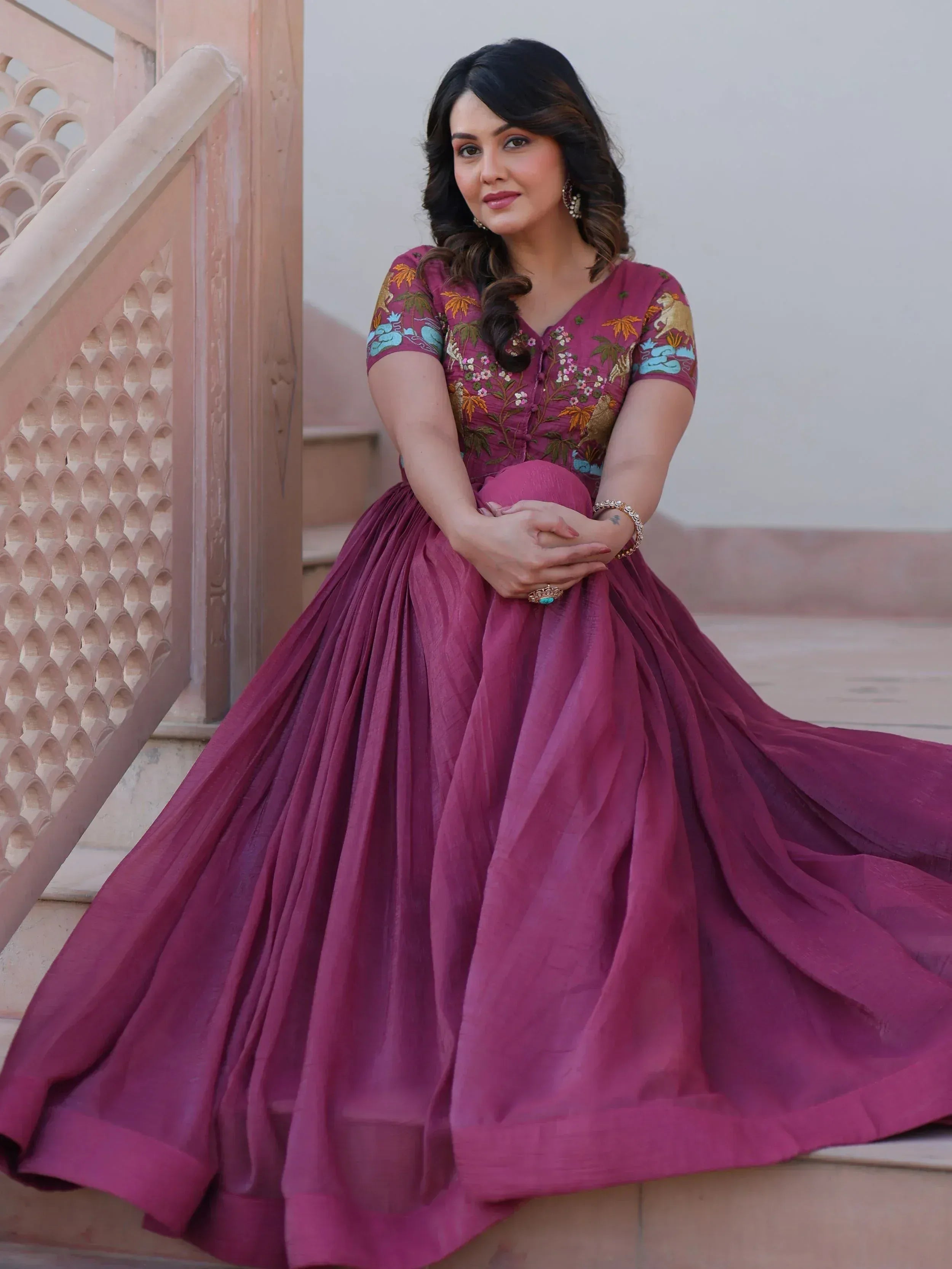 Woman in maroon embroidered ethnic gown with floral and animal motifs, perfect for Indian occasions.