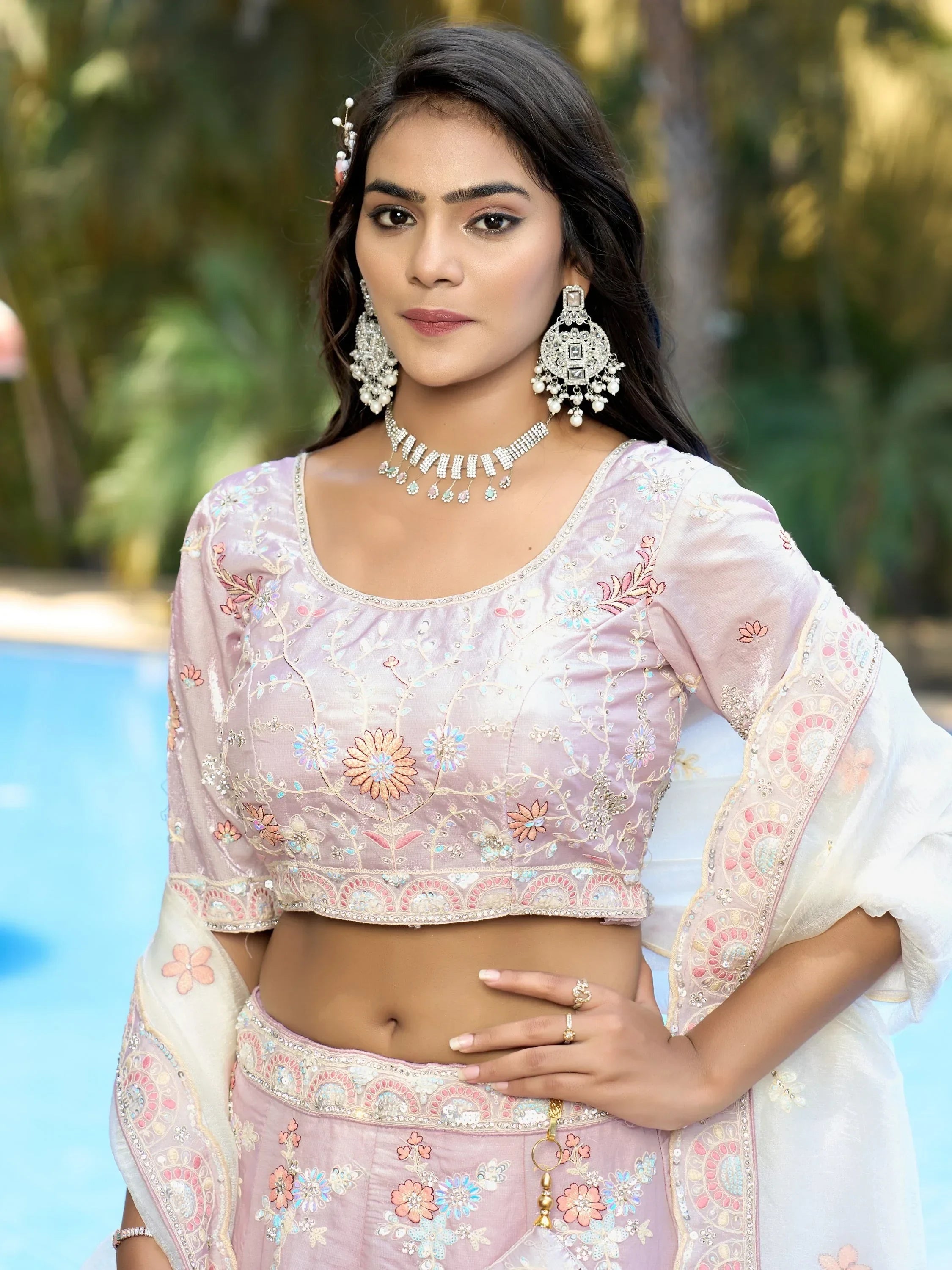 Woman in pink floral embroidered lehenga choli with statement jewelry by poolside