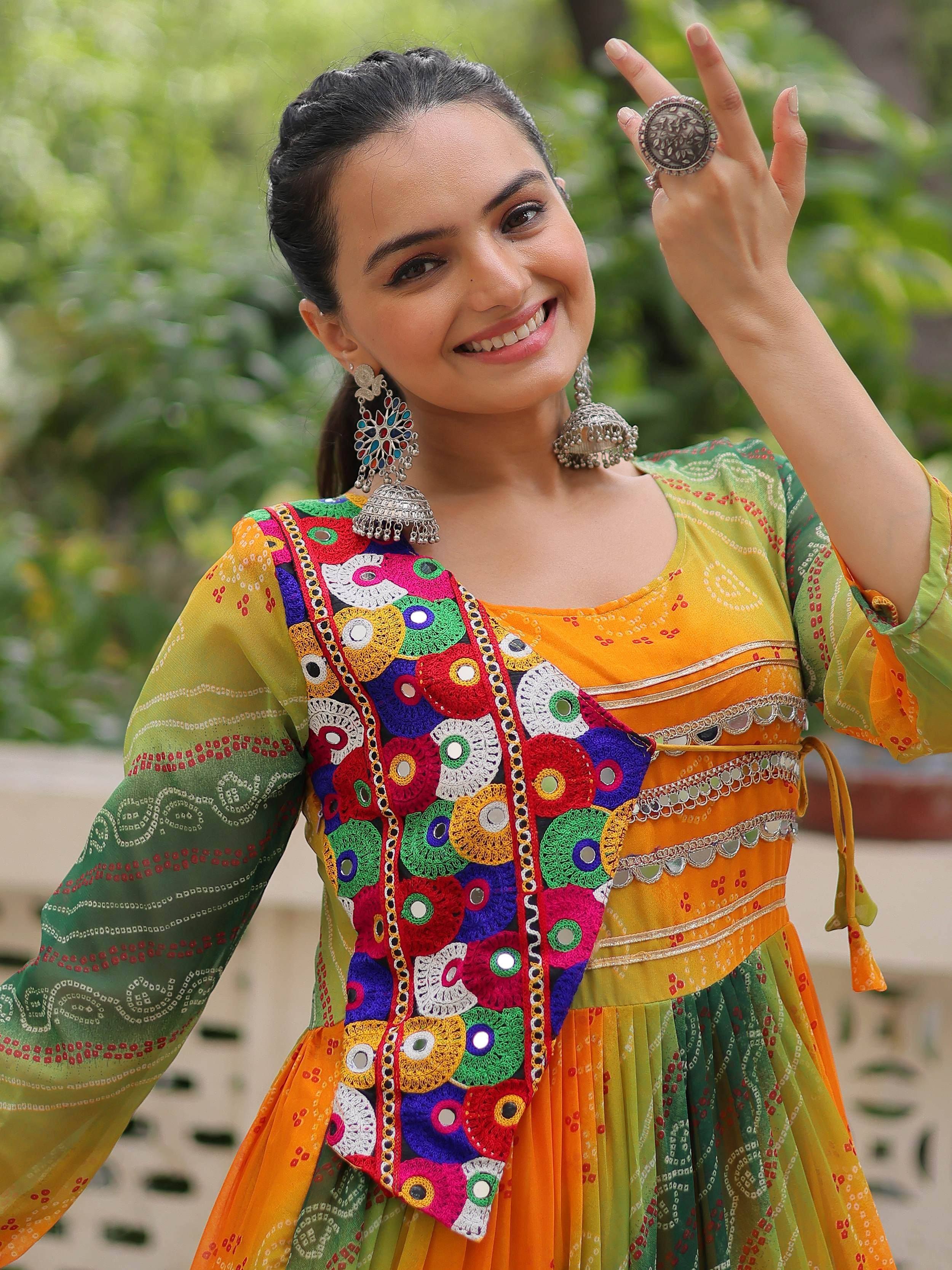 Woman in vibrant Indian ethnic gown with mirror work, jhumka earrings, and statement ring, perfect for festive occasions.