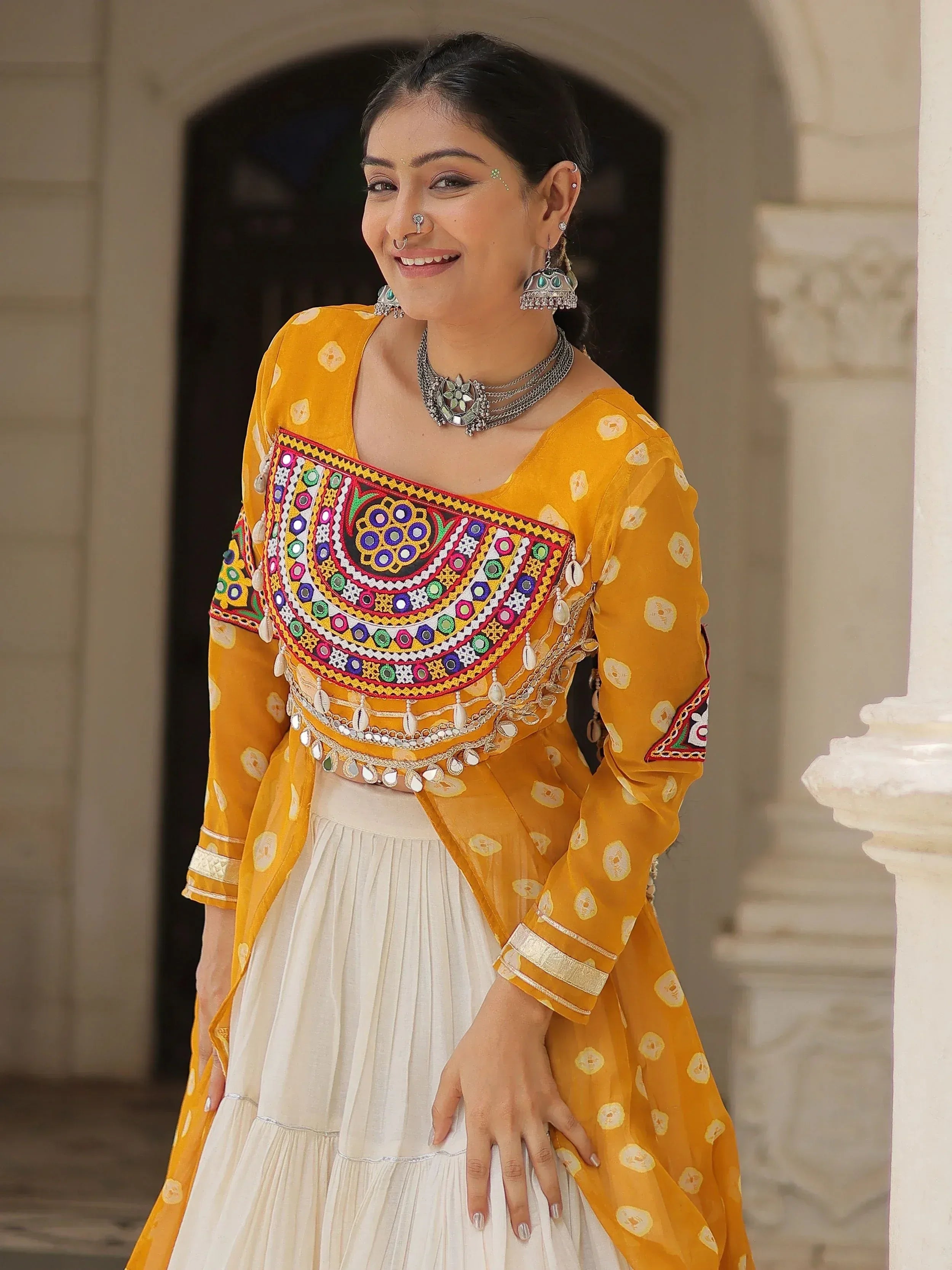 Woman in vibrant yellow ethnic top with mirror work and white skirt, traditional Indian attire
