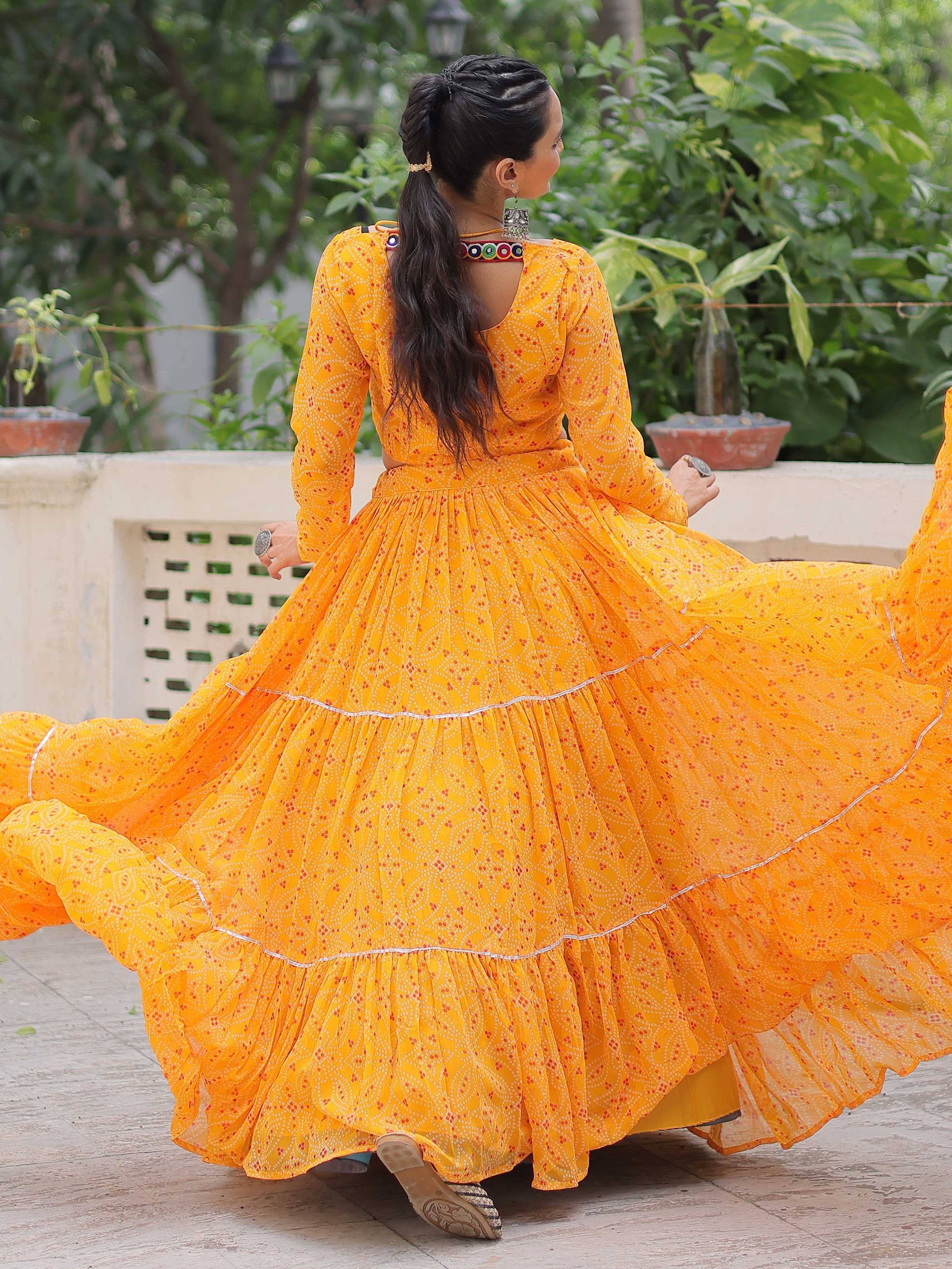 Woman twirling in vibrant yellow printed ethnic gown with flared skirt, perfect for festive occasions.