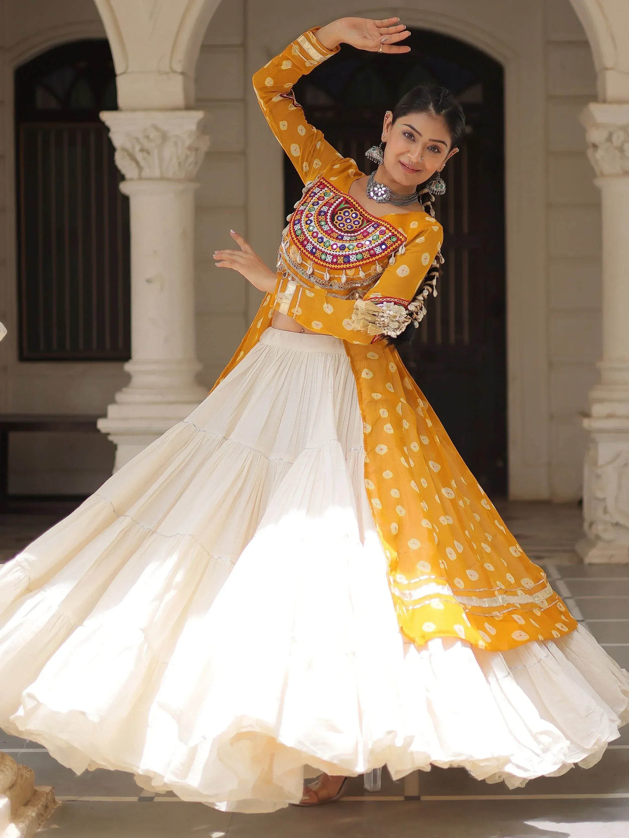 Woman in yellow embroidered choli and white lehenga dancing at courtyard