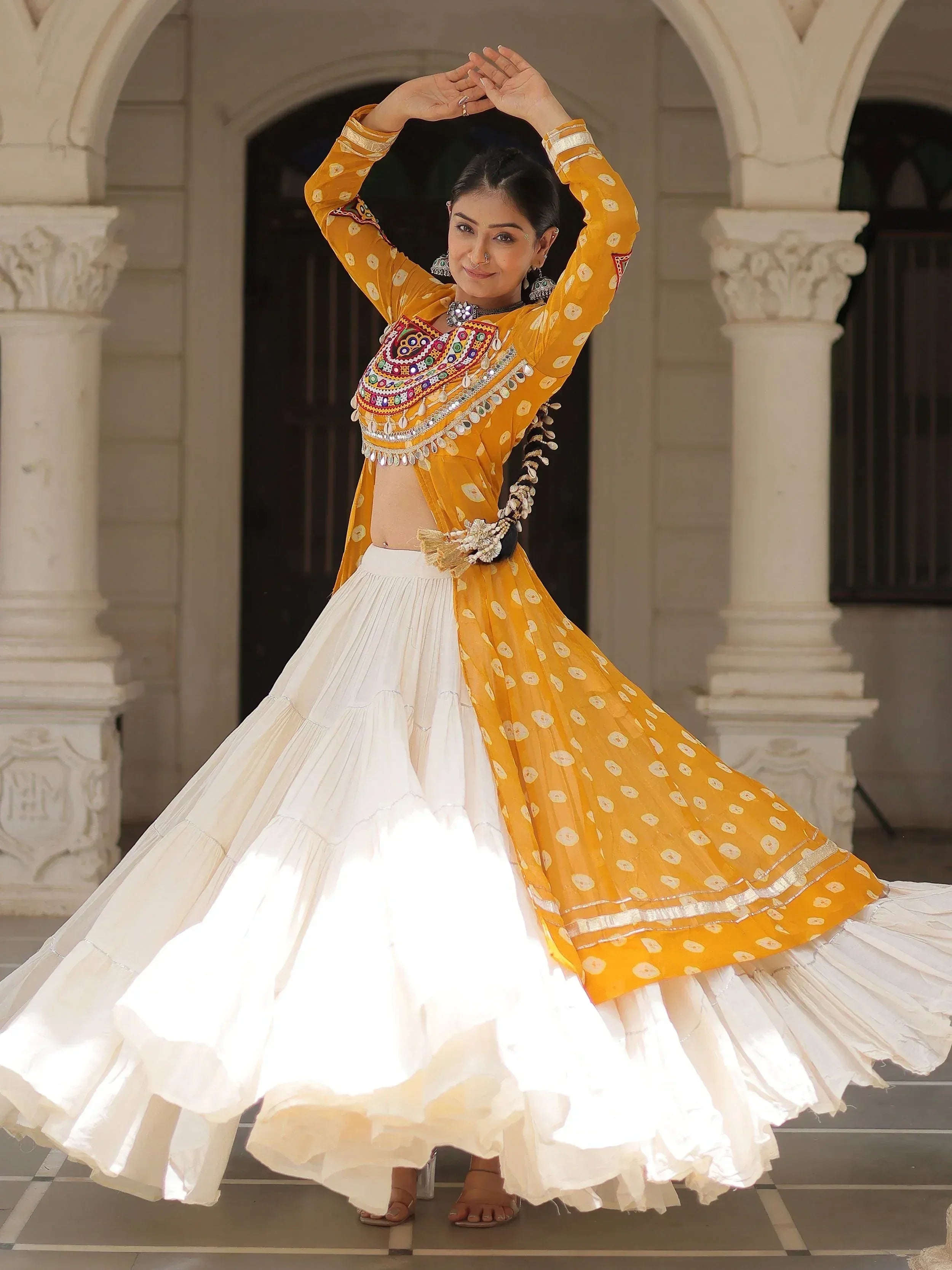 Woman in yellow and white ethnic lehenga choli with mirror work, dancing under arched doorway