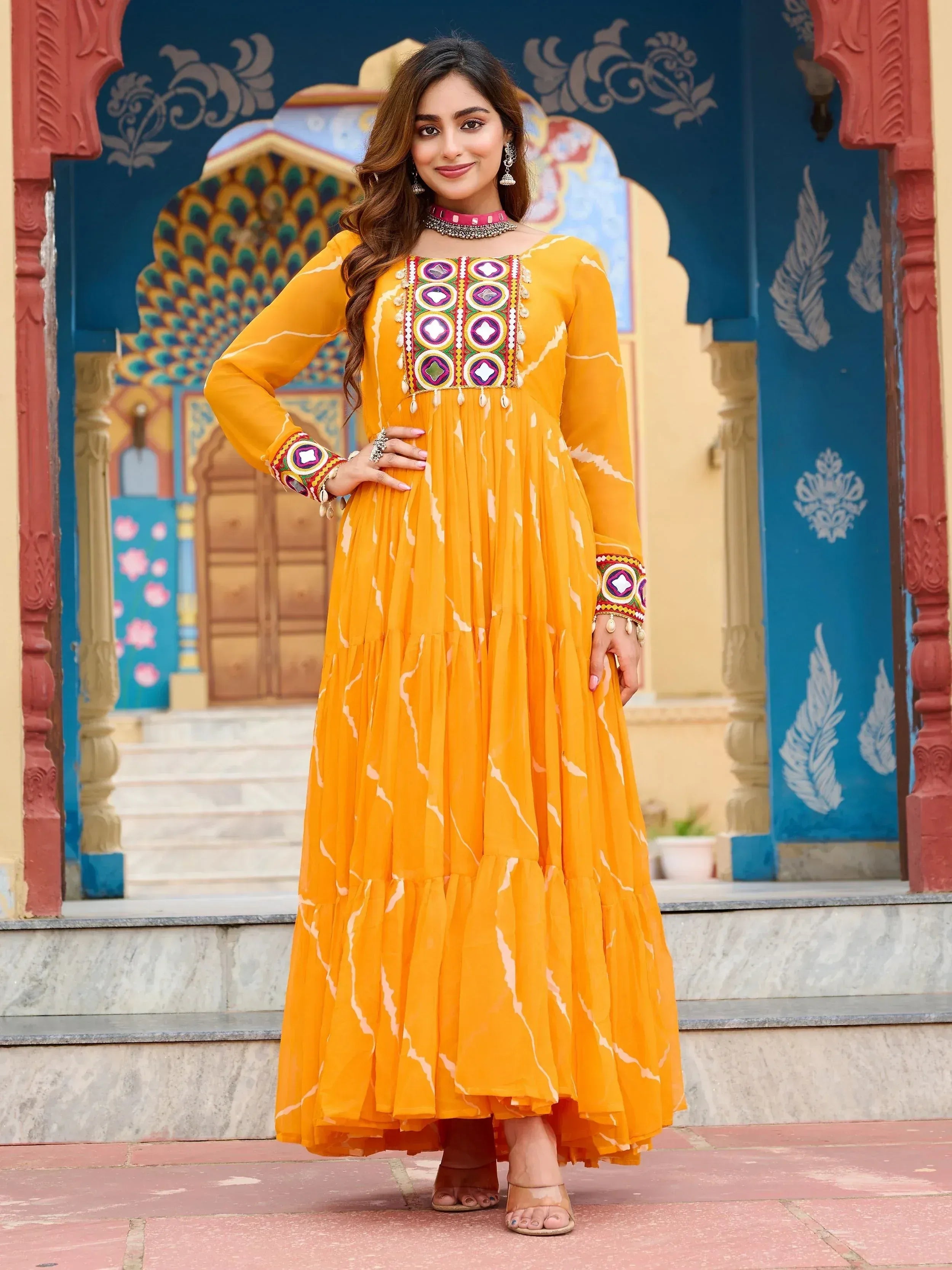Woman in vibrant yellow ethnic gown with mirror work, perfect for Indian occasions and festive wear.