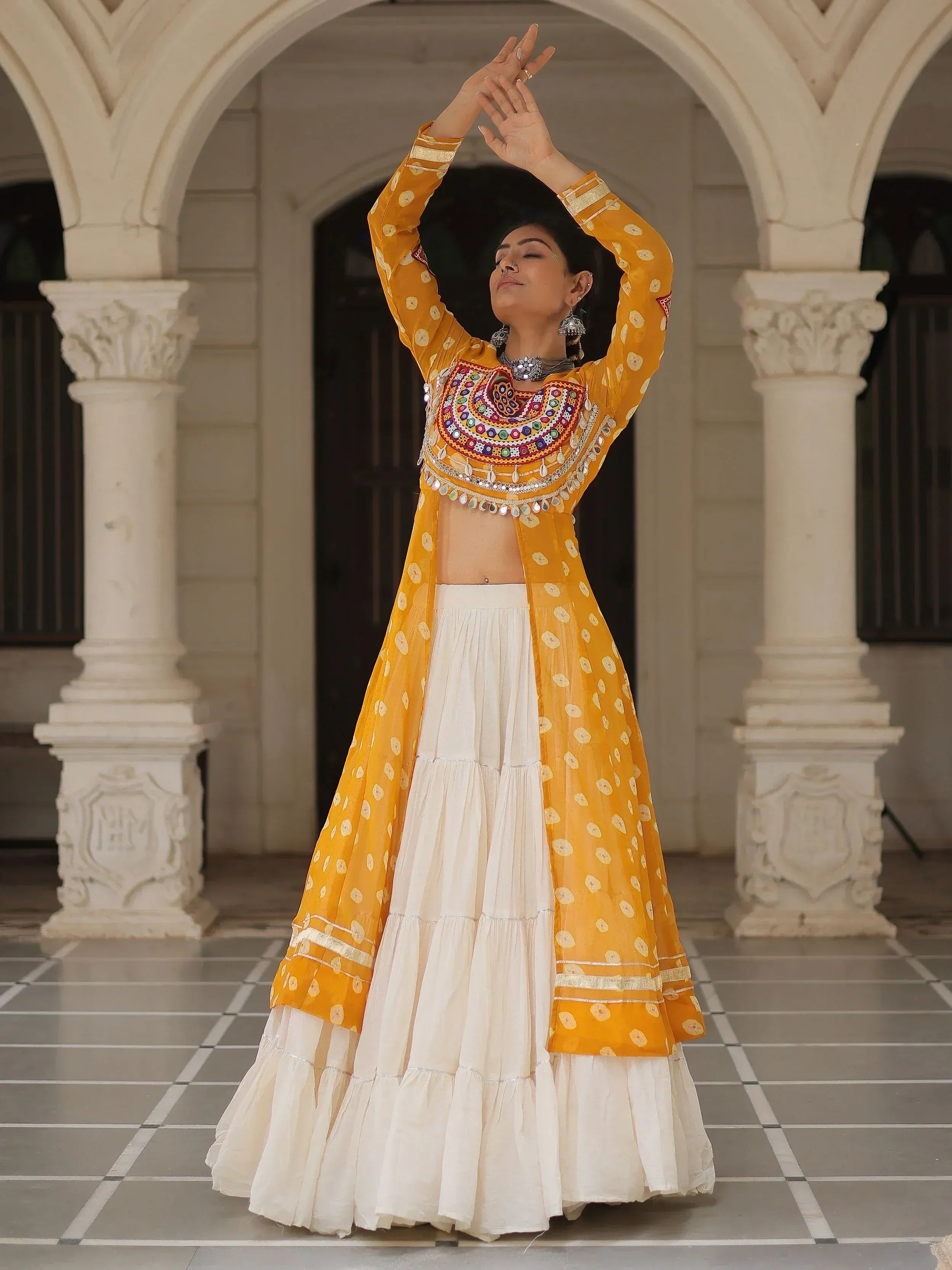 Woman in yellow and white ethnic lehenga choli with mirror work, dancing under arched courtyard