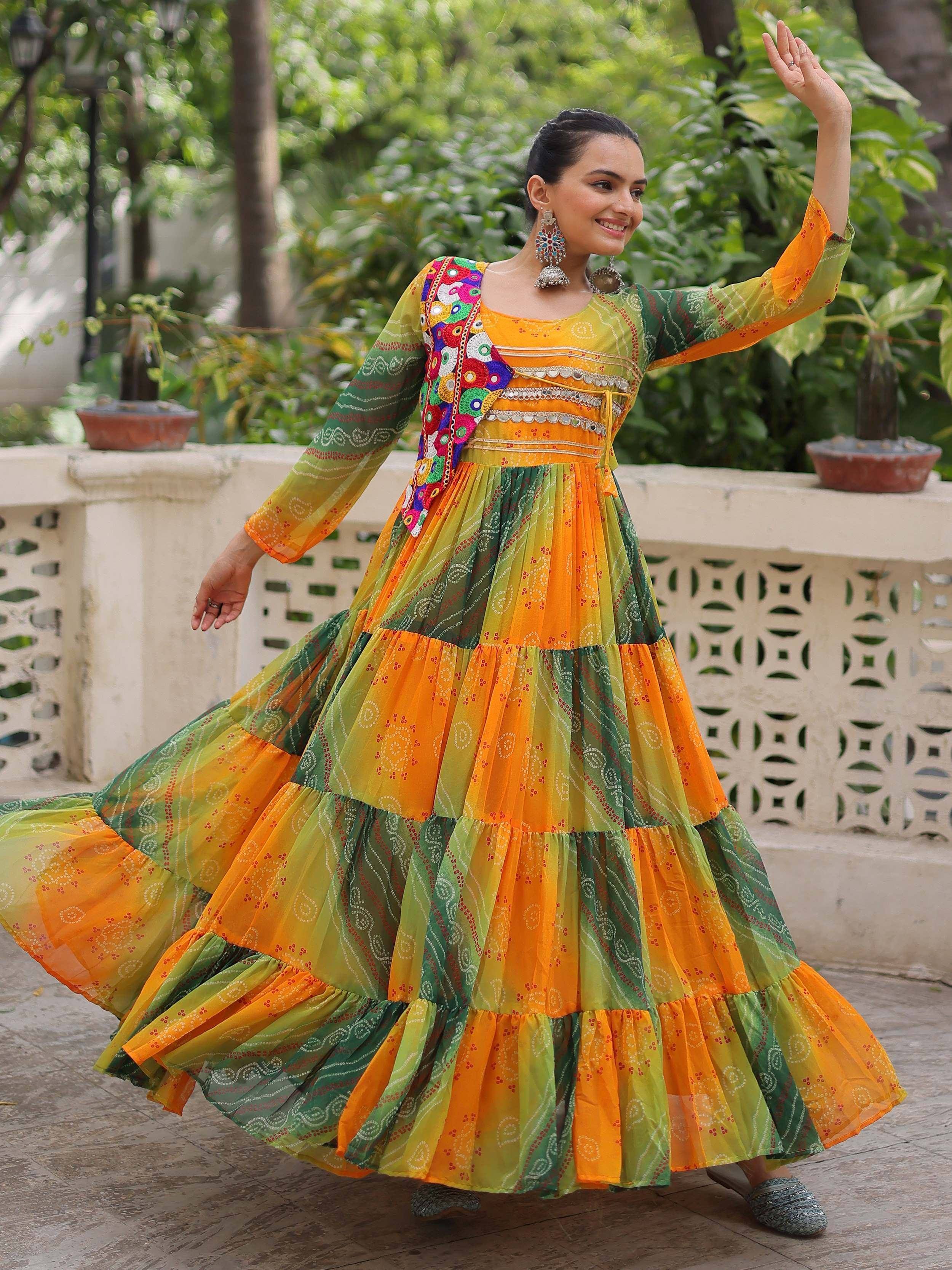 Woman in vibrant orange and green tiered ethnic gown with mirror work, perfect for festive occasions.