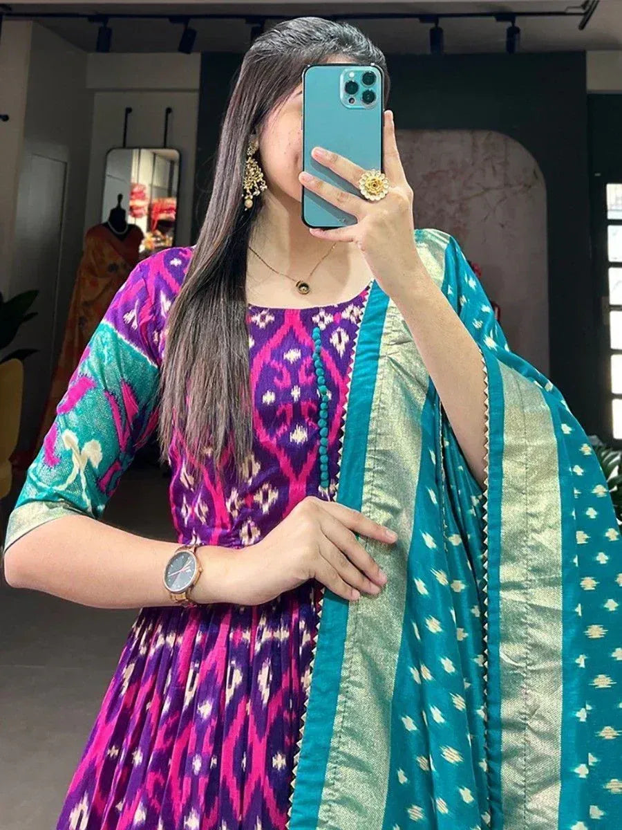 Woman in vibrant purple and teal ikat print ethnic gown with matching dupatta, perfect for Indian occasions.