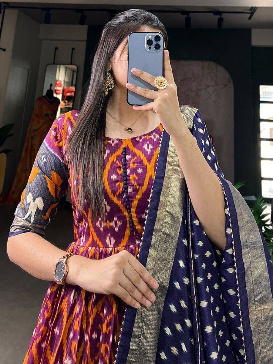 Woman in vibrant purple and orange ikat print ethnic gown with matching dupatta, perfect for Indian occasions.