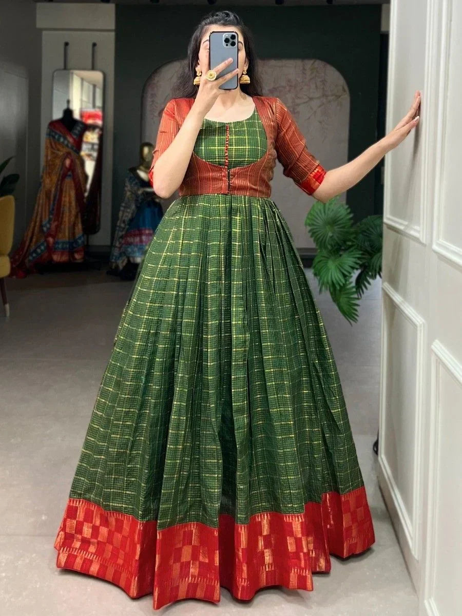 Woman in green and rust orange traditional gown with gold checks and red border, taking a selfie indoors