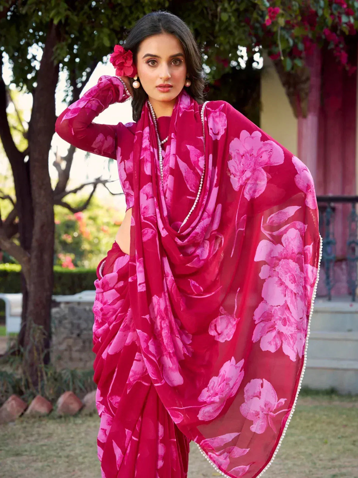 Vibrant pink floral saree with pearl trim, styled with matching blouse and floral hair accessory