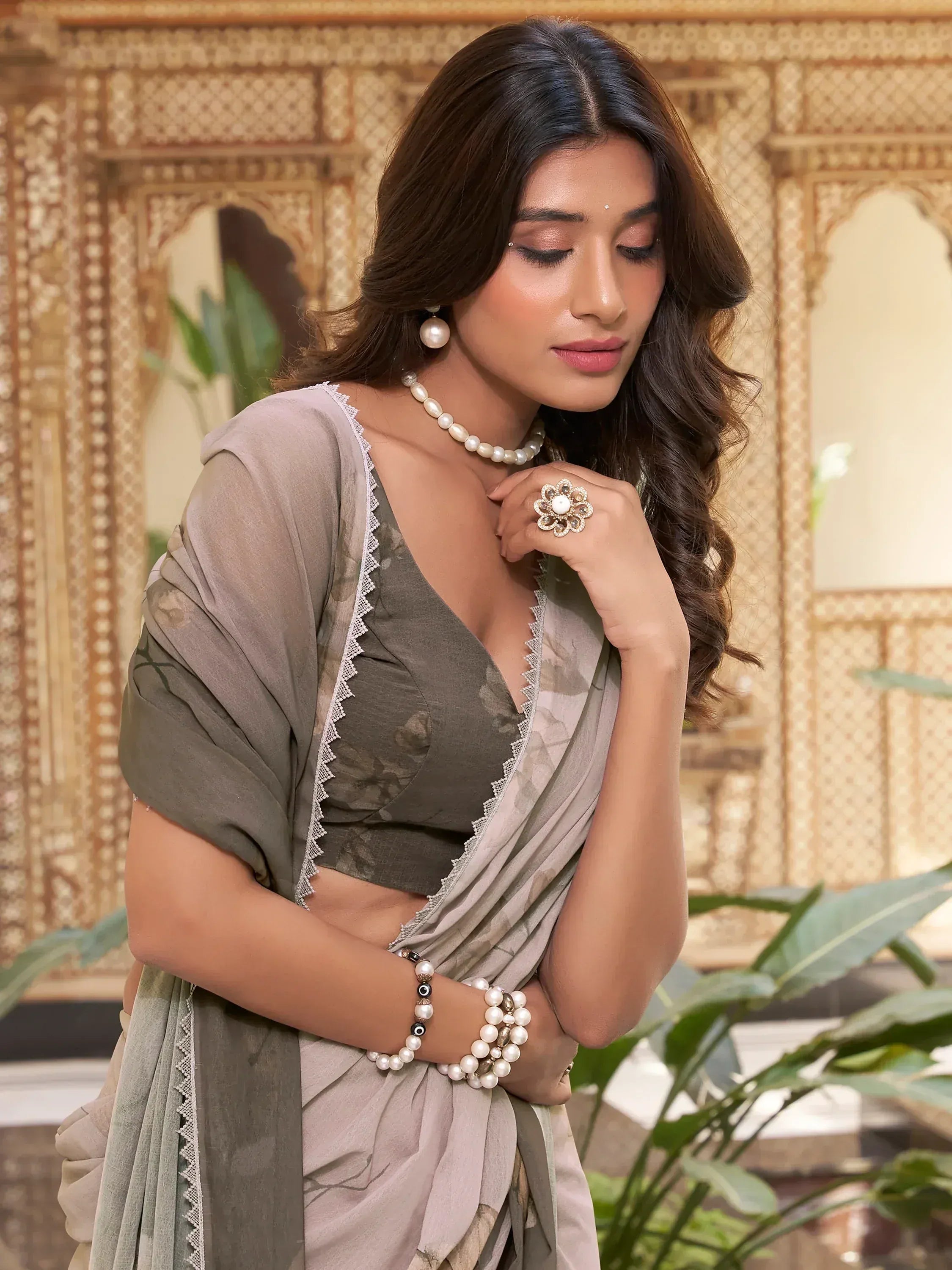 Elegant woman in olive green floral saree with lace trim, pearl jewelry, and traditional Indian styling.
