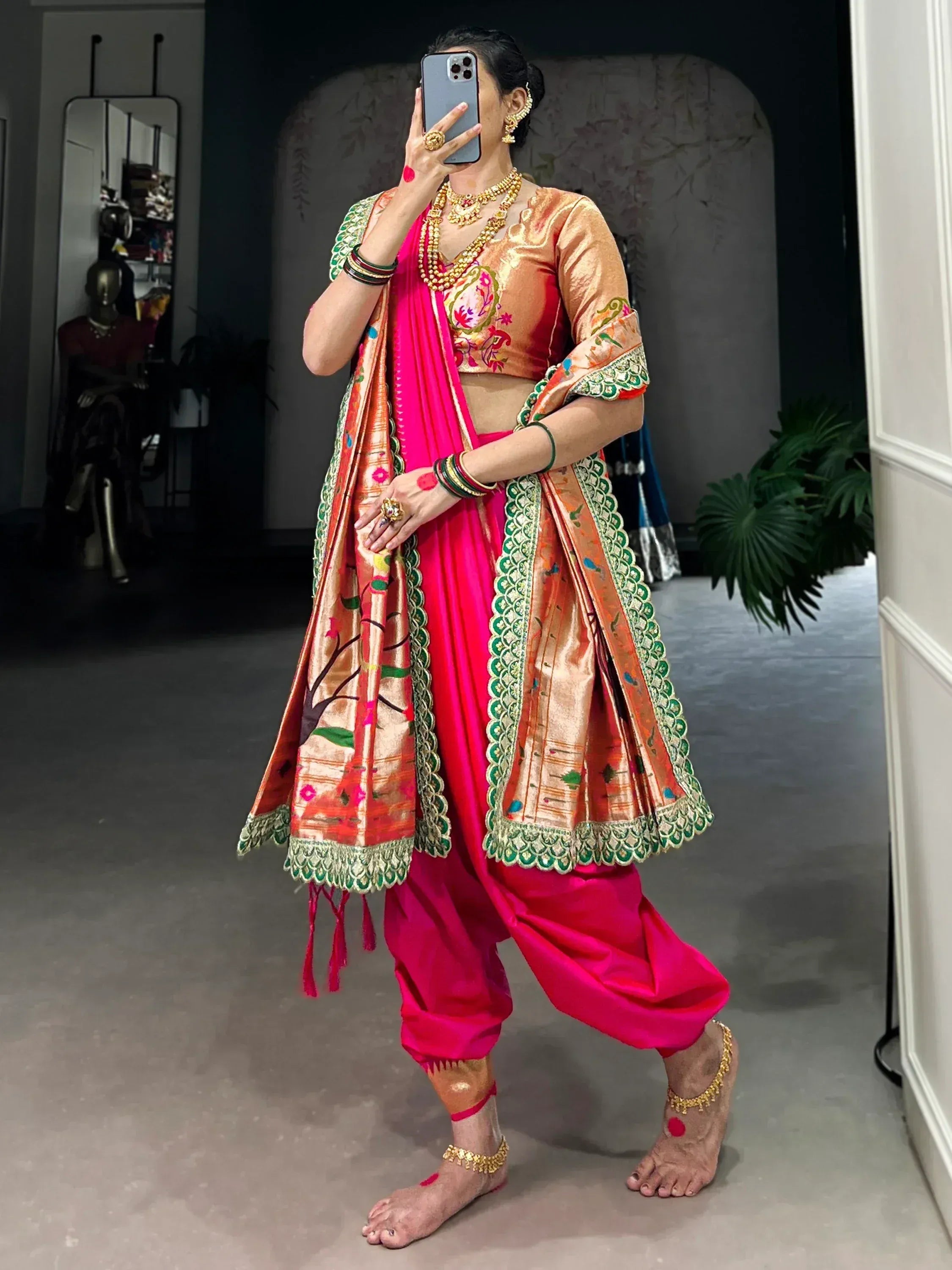 Woman in vibrant pink and gold designer lehenga choli with intricate embroidery and traditional jewelry.